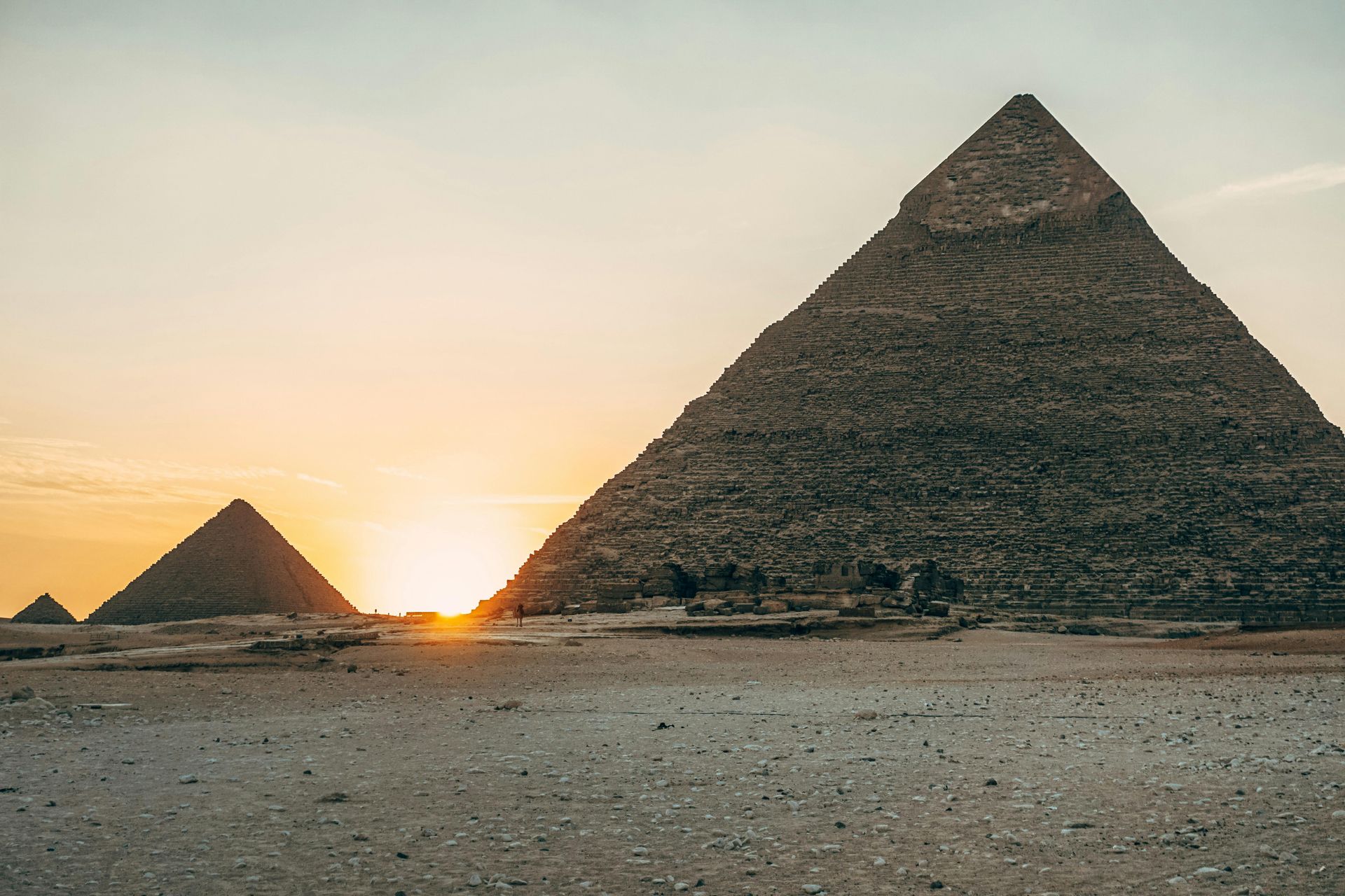 The sun is setting behind two pyramids in the desert.