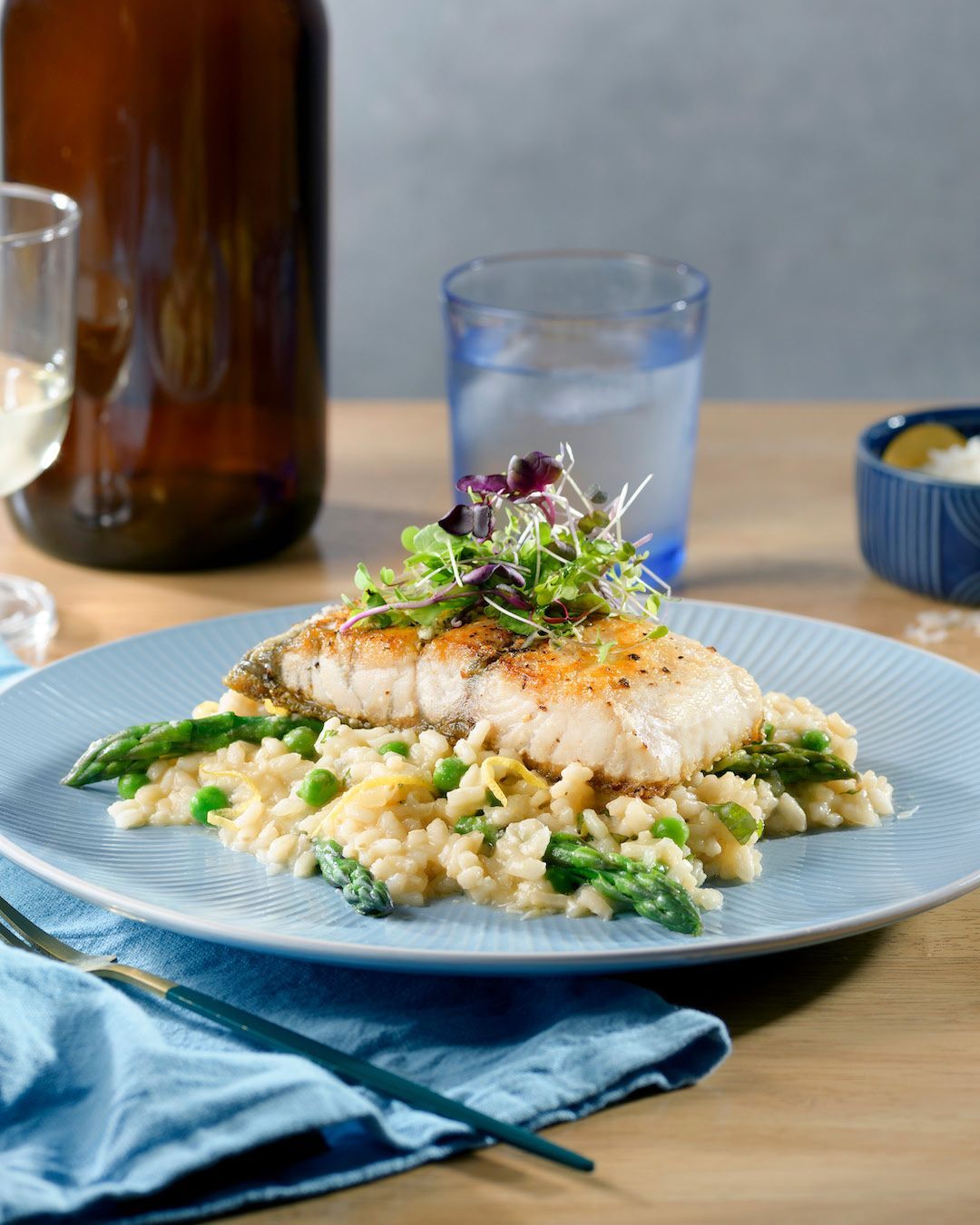 A piece of seared white fish served over pea and asparagus risotto on a blue plate, topped with fresh microgreens.