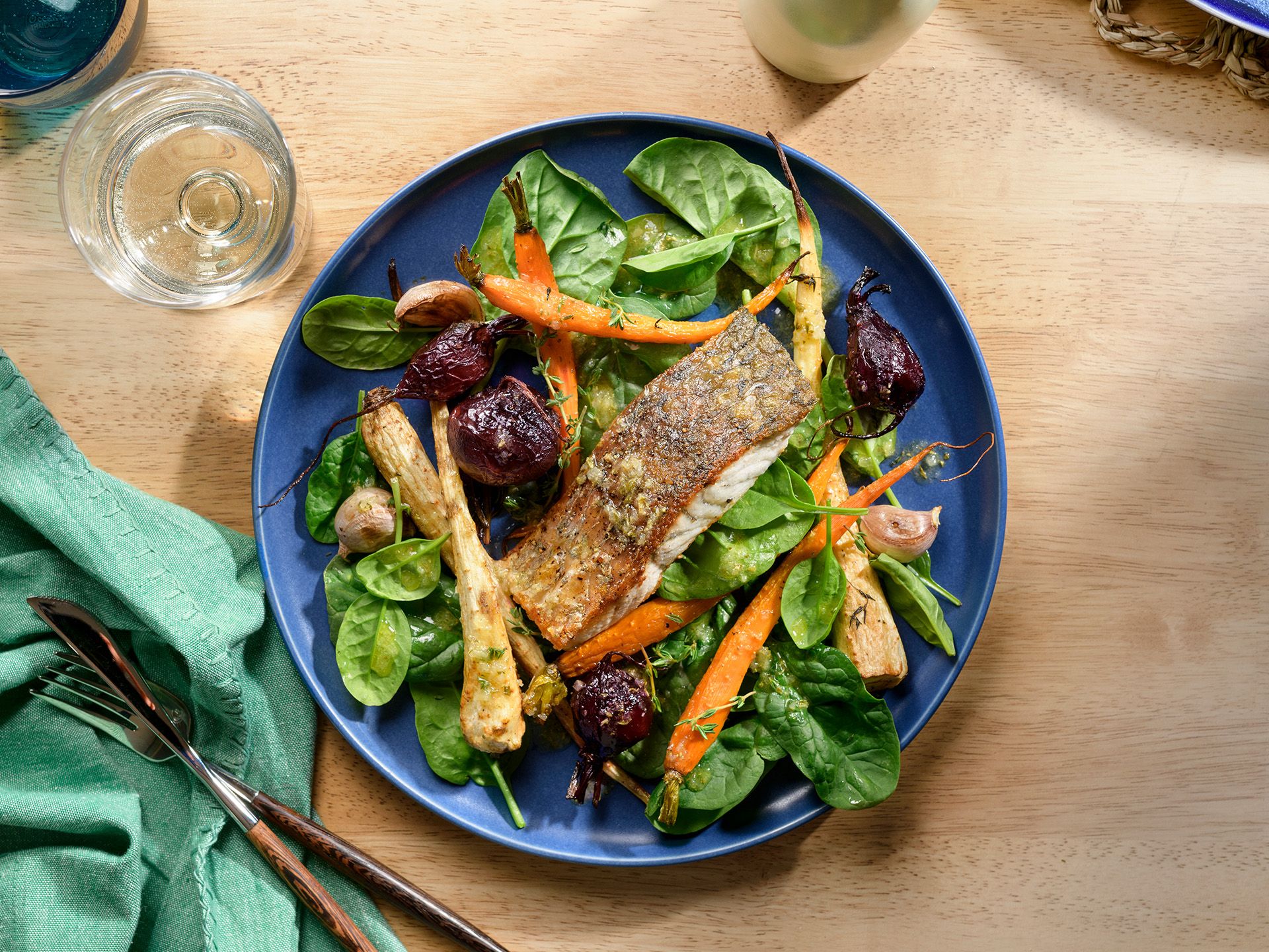 A blue plate featuring a pan-seared salmon fillet over a bed of spinach, roasted carrots, and beets on a wooden table.