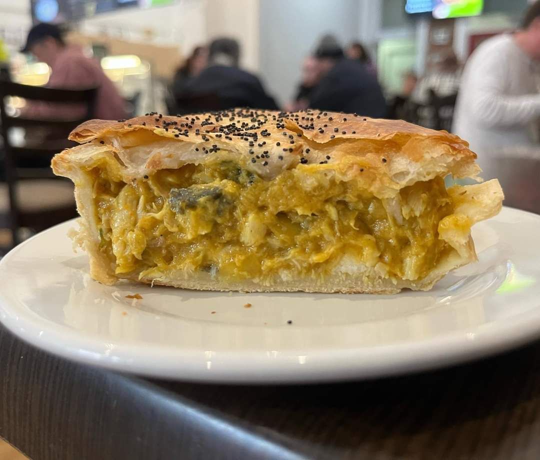 A cross-section of a savory pot pie with a flaky, seeded crust and a creamy, yellow vegetable filling on a white plate.