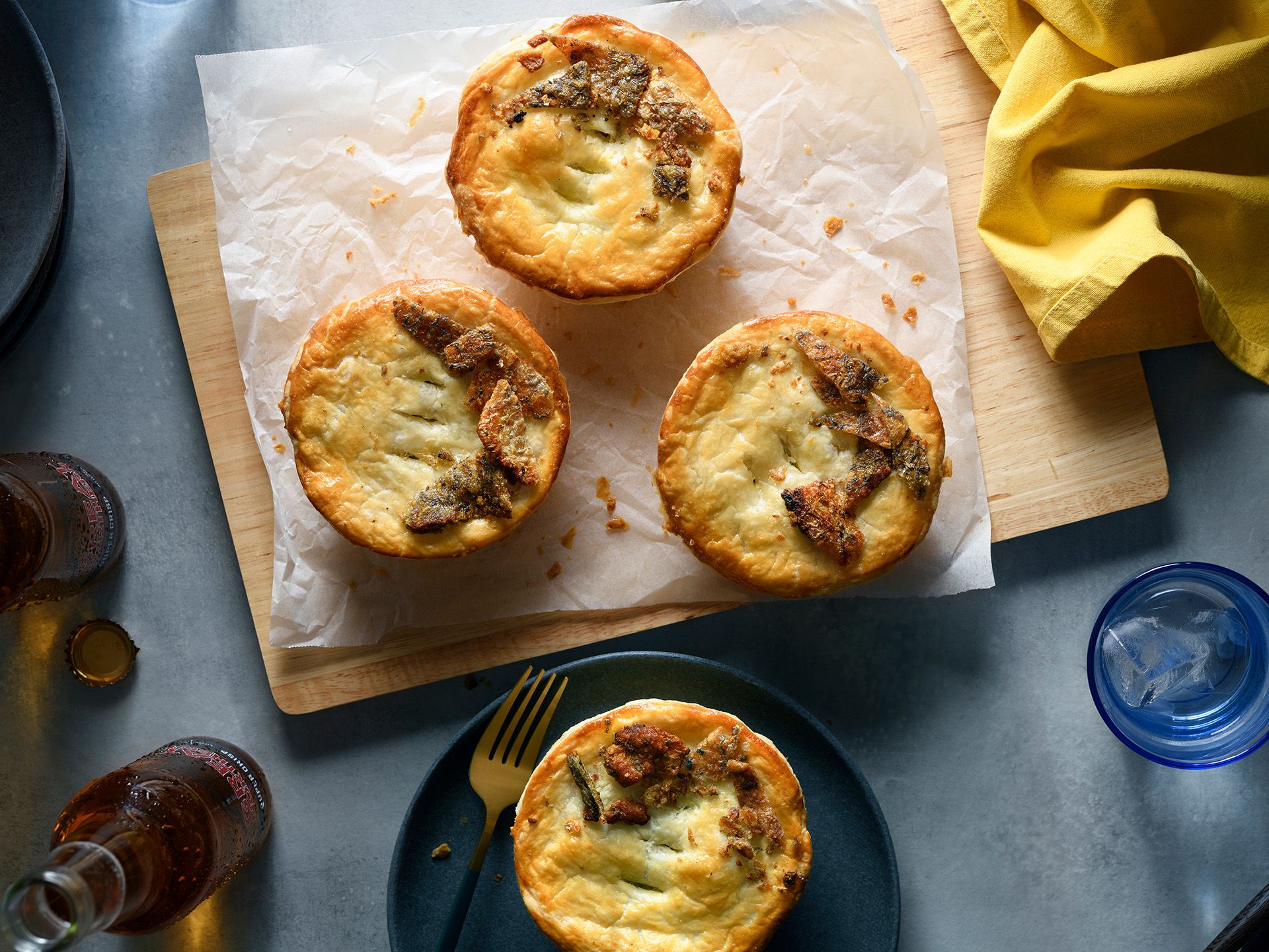 Four golden-brown savory pies with decorative pastry crusts served on a wooden board and a dark plate with a fork.