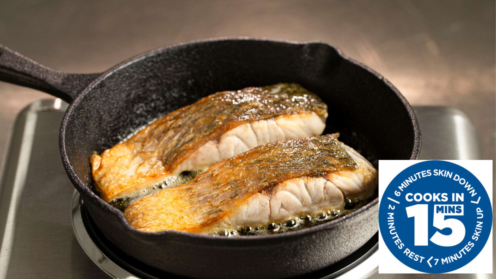 Two fillets of fish searing in a black cast iron skillet on a stovetop, with a badge reading 
