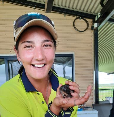 A person in a neon yellow and navy work shirt smiling while holding a small, dark bird in their hands on a patio.