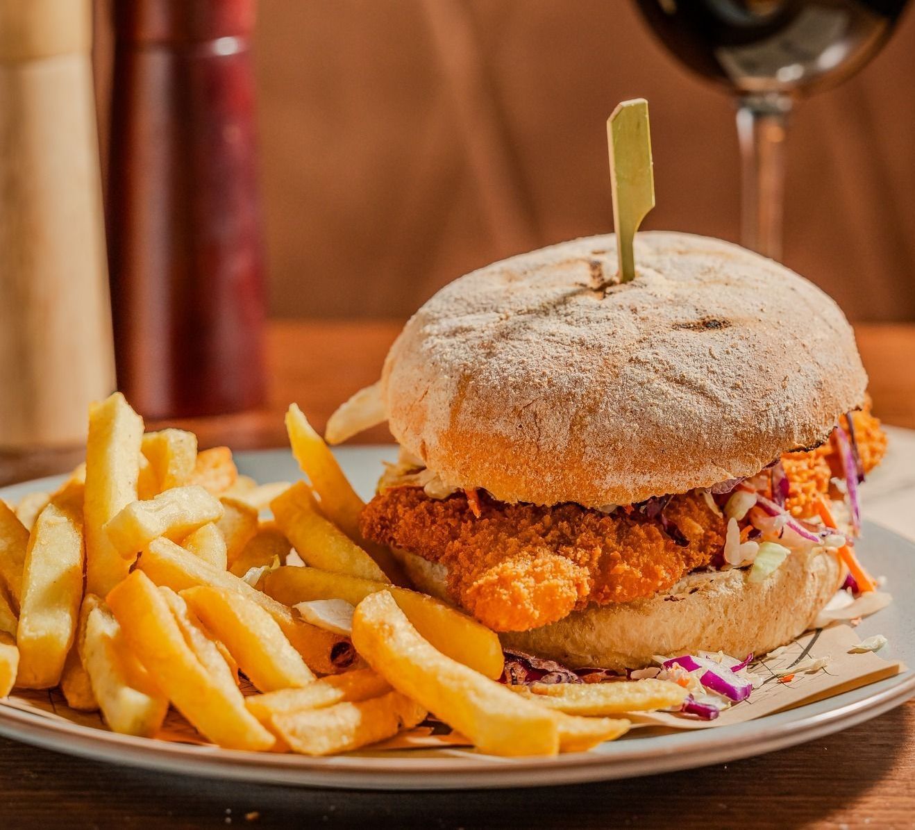A fried chicken sandwich with coleslaw on a bun, served with a side of golden french fries on a plate.