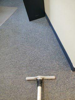 Vacuum cleaner head on gray carpet beside a hallway wall with blue baseboard trim