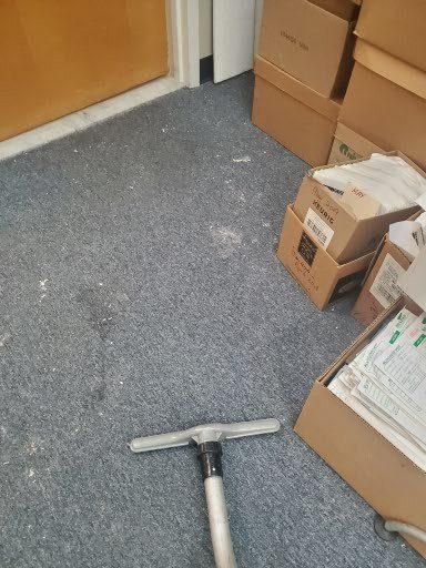Carpeted office floor with a vacuum head near stacked cardboard boxes and a door.