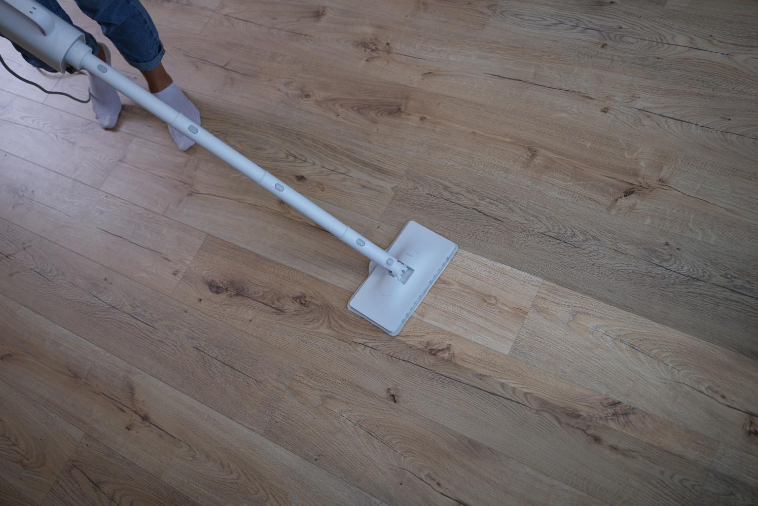 Person using a white vacuum mop on a light wood floor