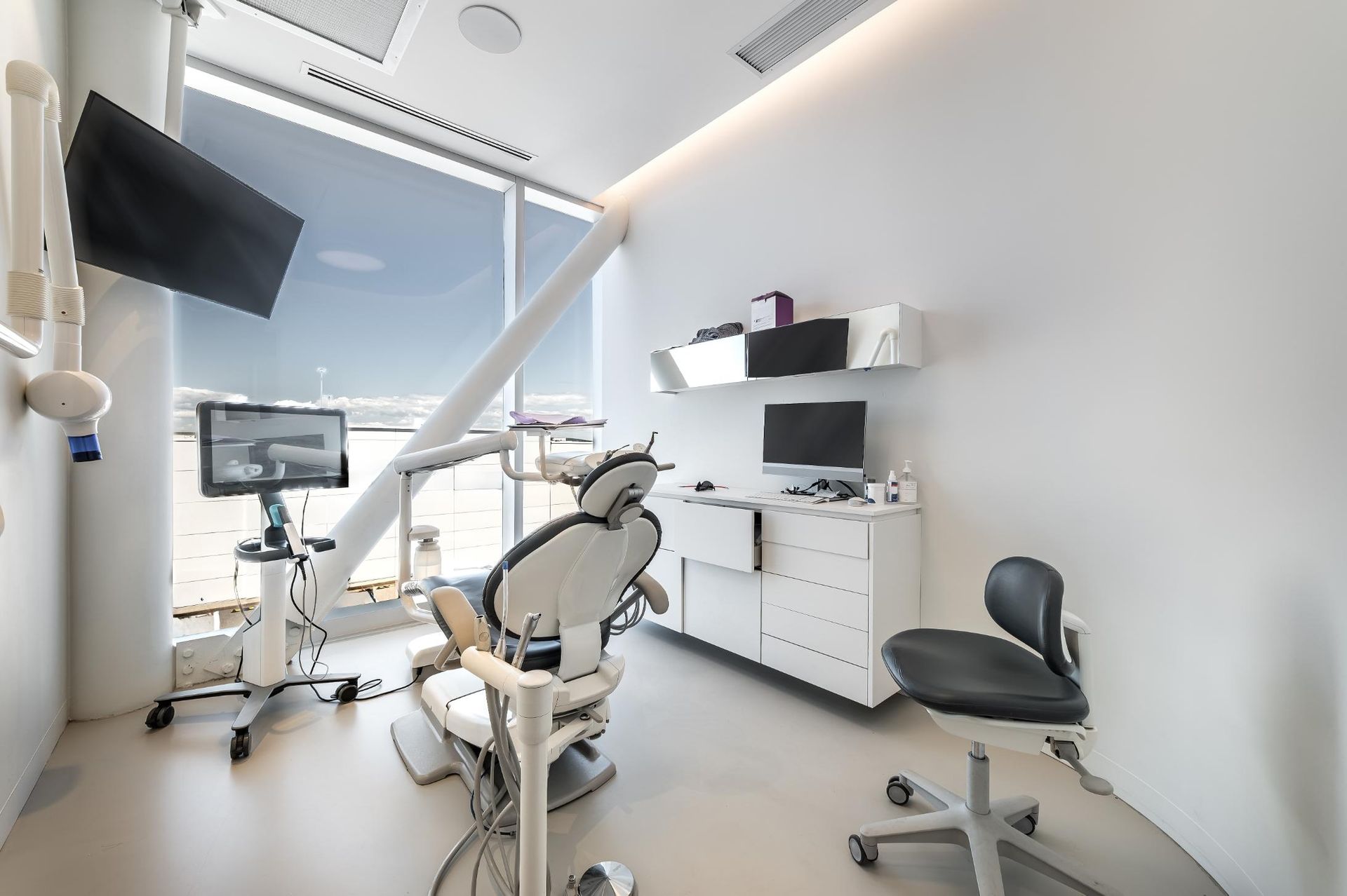 Modern dental exam room with chair, monitor, and treatment equipment in a bright white space