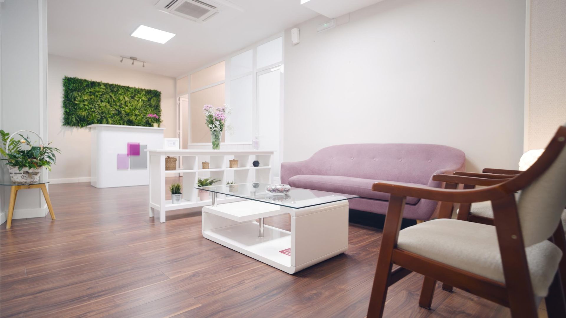 Bright modern living room with a lavender sofa, white coffee table, wooden floor, and chairs by a large window.