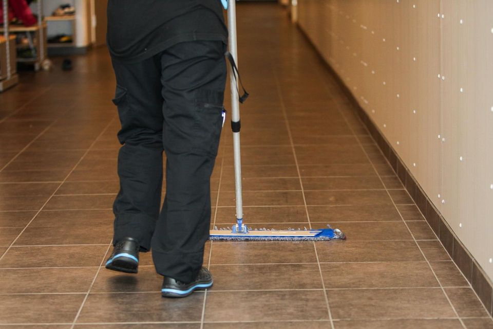 Person mopping a tiled hallway floor with a blue mop