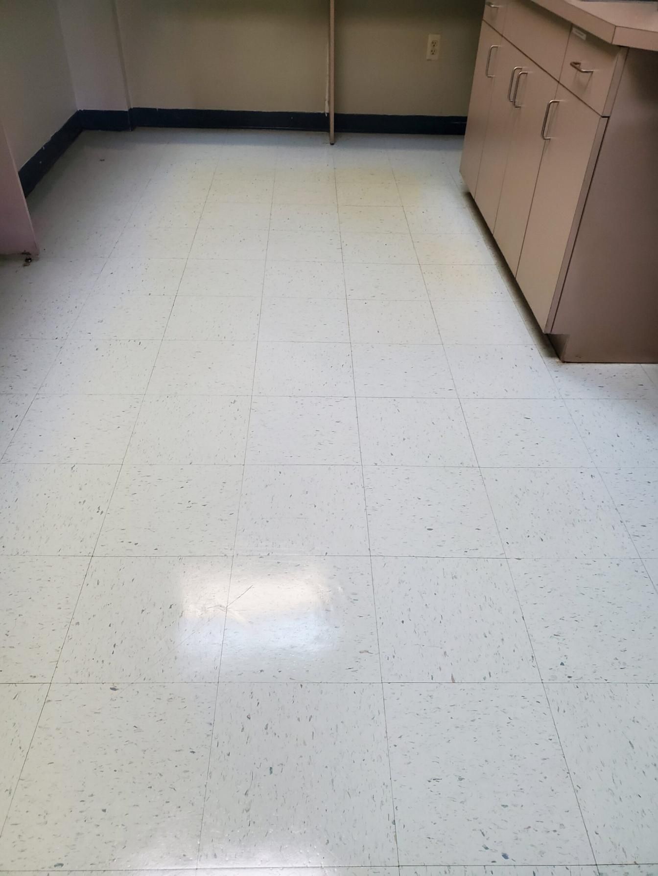 Empty beige office or kitchen floor with white speckled tiles and cabinets along the walls