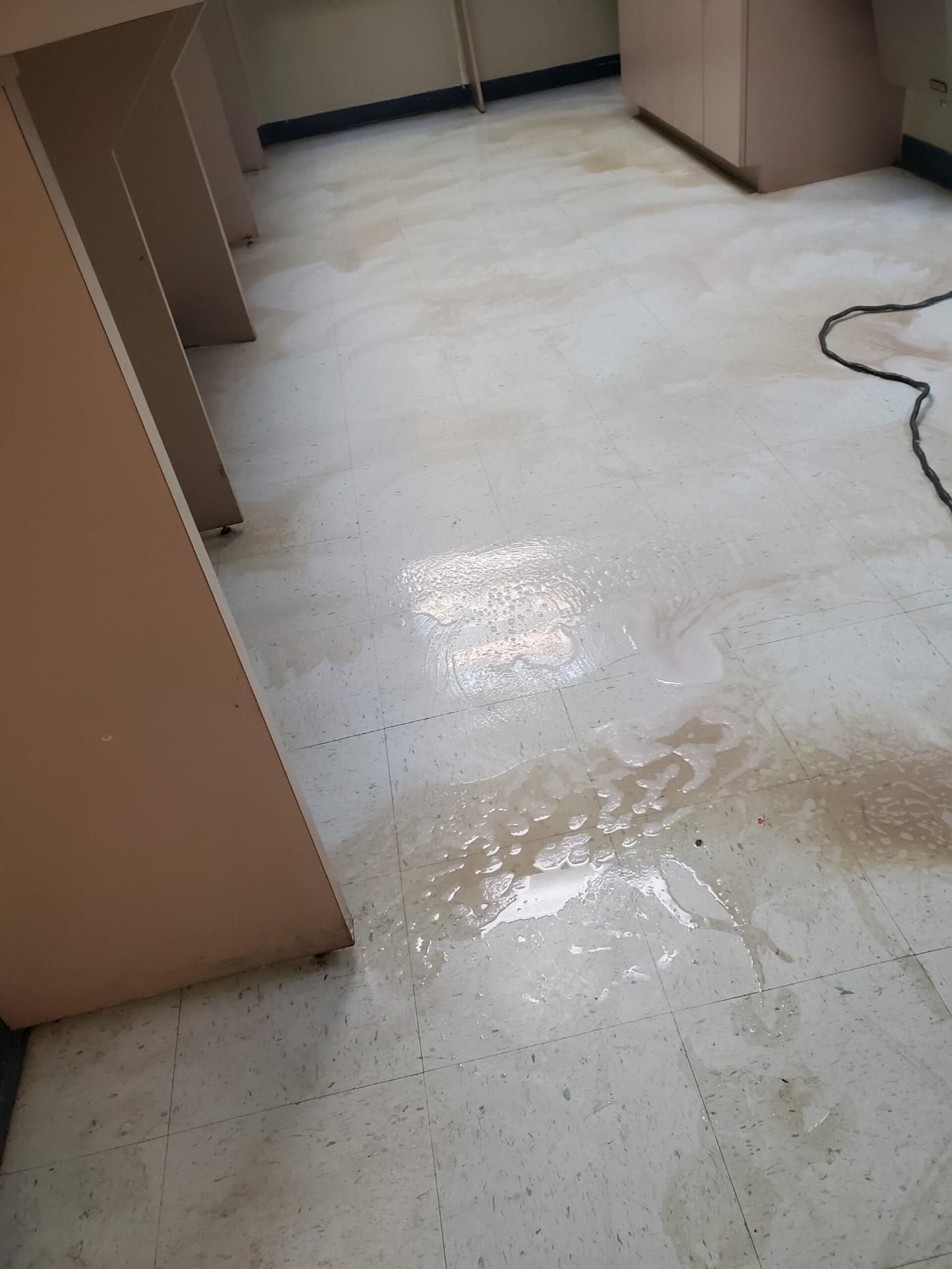 Spilled liquid on a white floor in a hallway or kitchen, with cabinets along the sides.