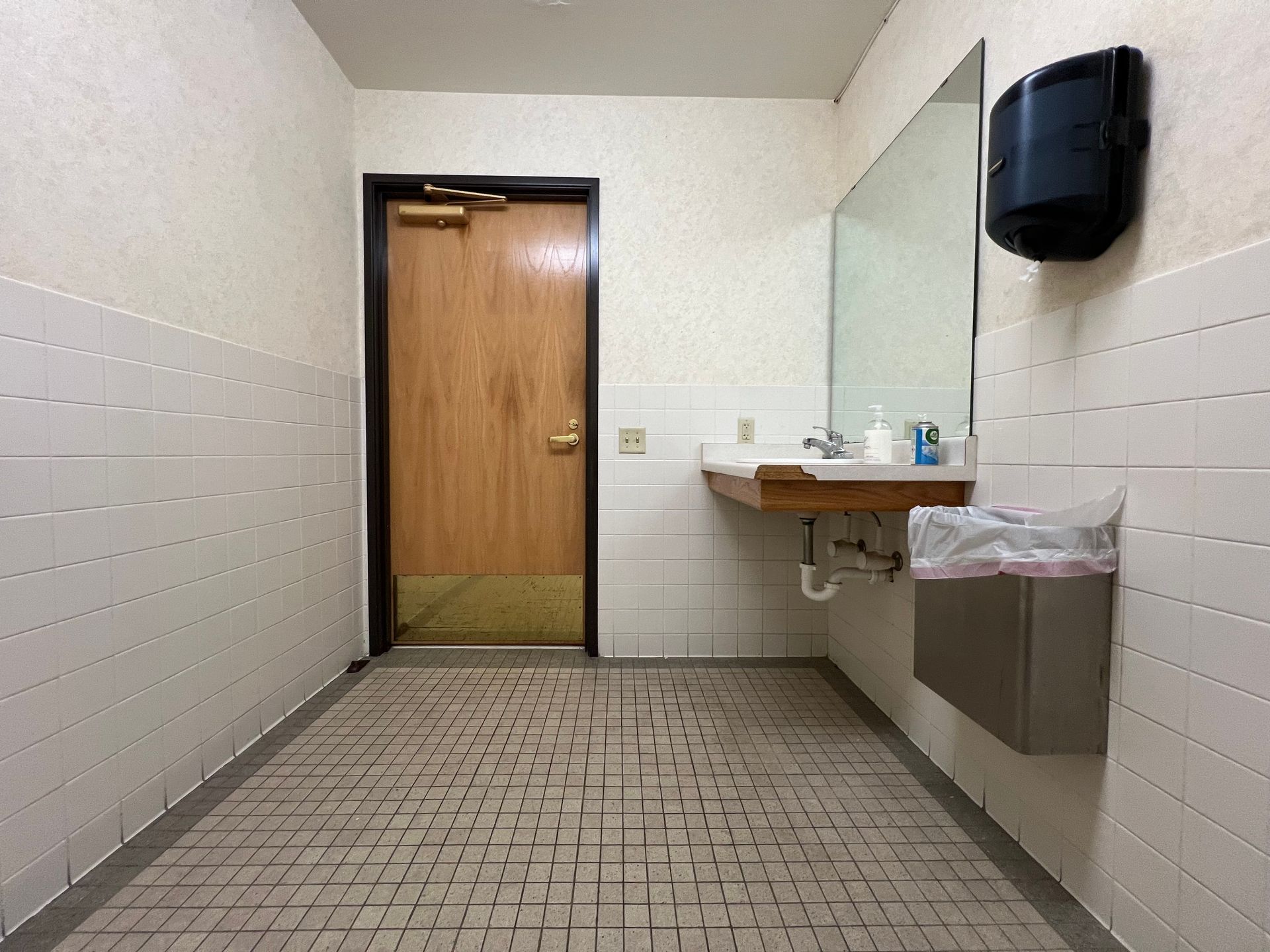 Gloved hand using a black-and-yellow steam cleaner on white tile grout in a bathroom.