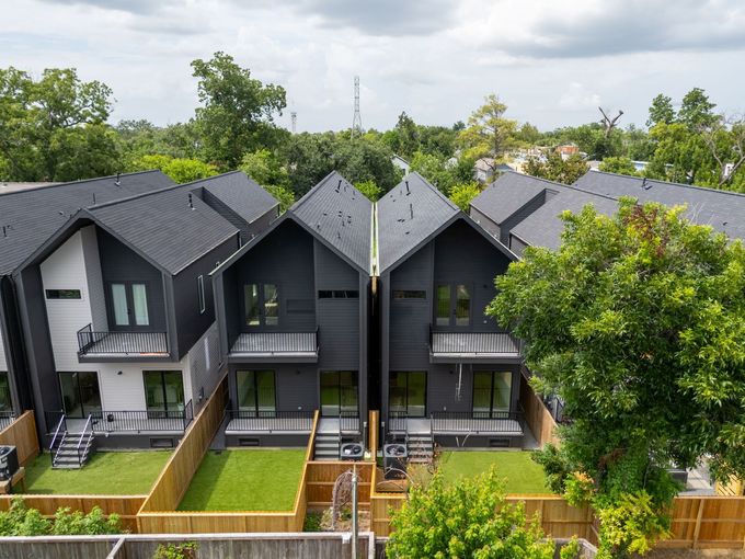 Row of modern gray townhouses with fenced front yards and green trees in front