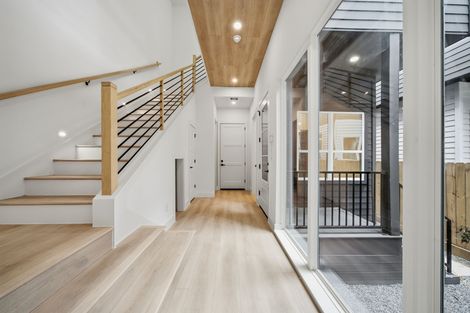 Modern bright hallway with light wood floors, white staircase, and glass wall overlooking a patio.