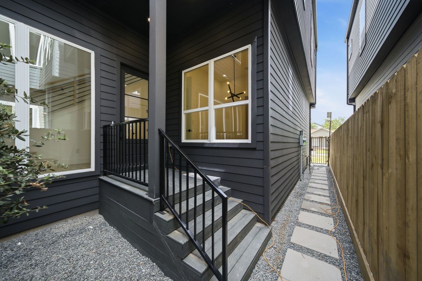 Narrow side walkway between dark gray houses with steps, gravel, and a wooden fence on the right.