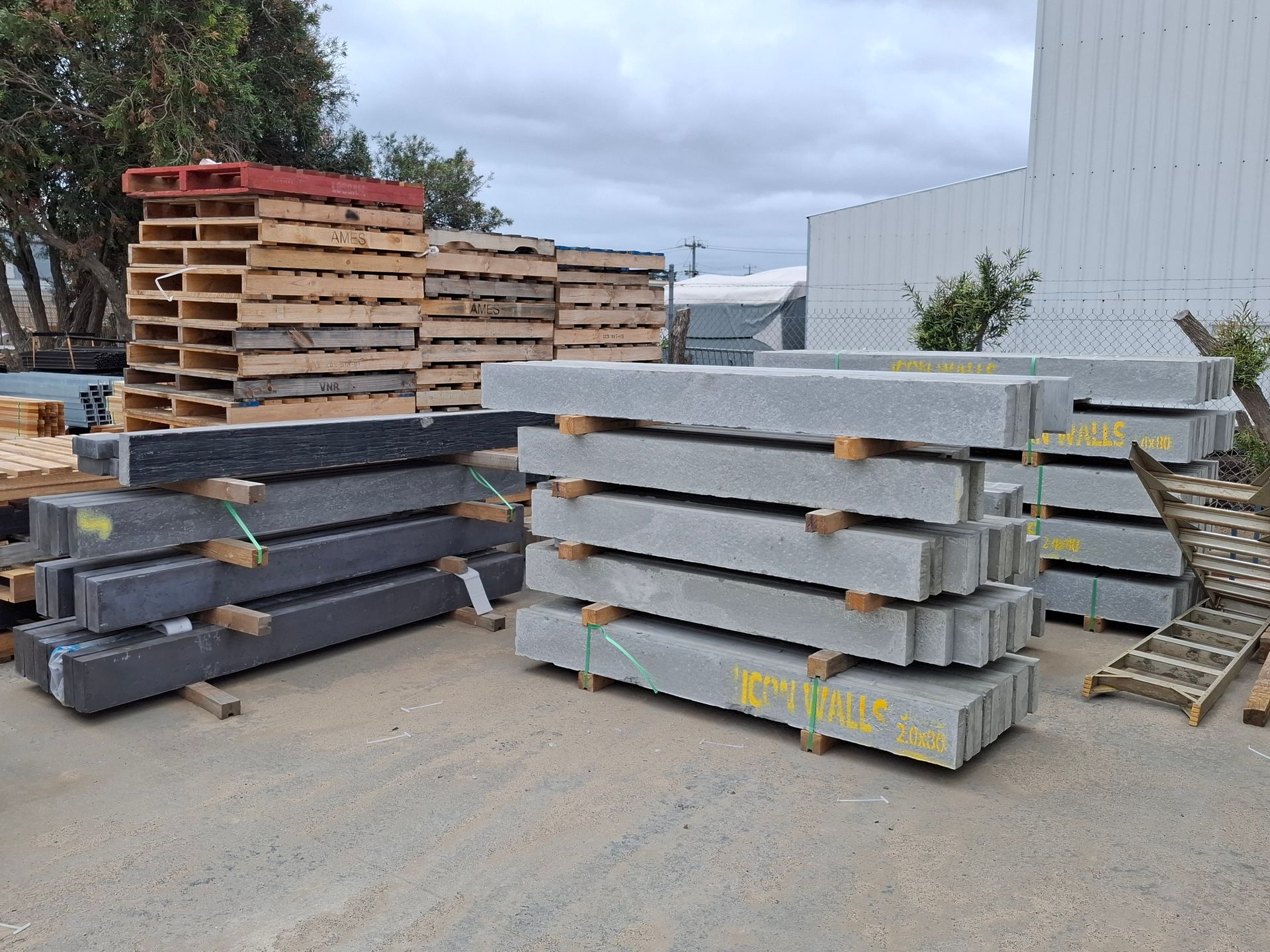 Stacks of granite and timber beams in an outdoor industrial setting, alongside wooden pallets.