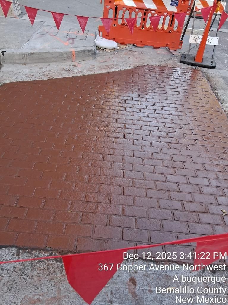 Wet red brick sidewalk beside orange construction barriers and cones in a street scene