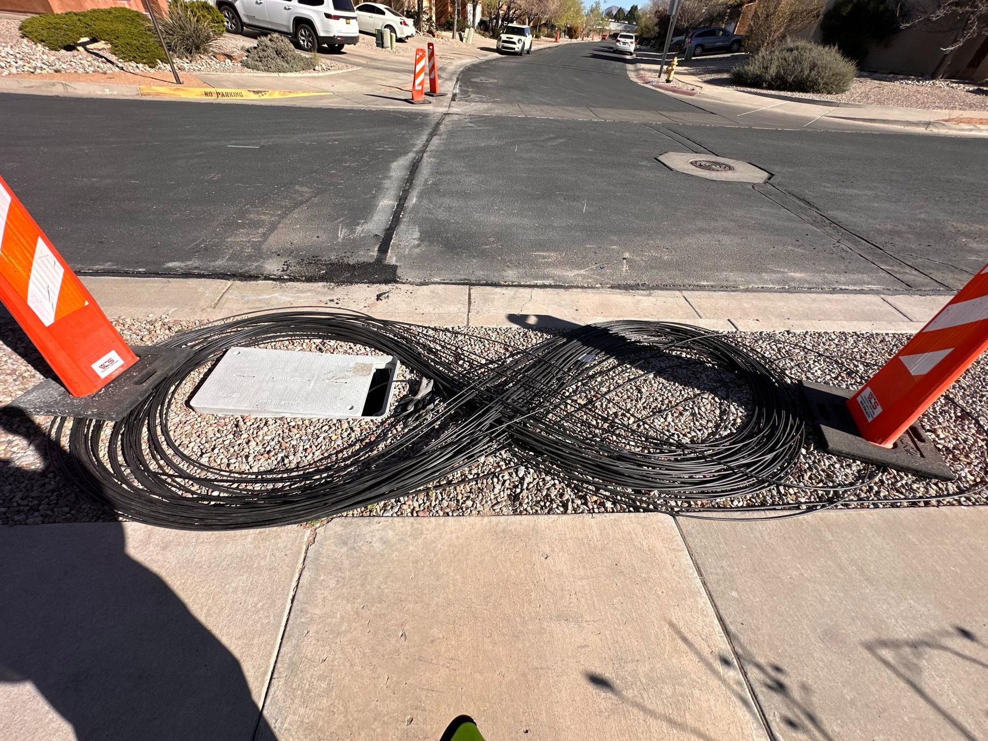 Burned black cable across sidewalk near orange cones and a street, with charred debris and a utility cover