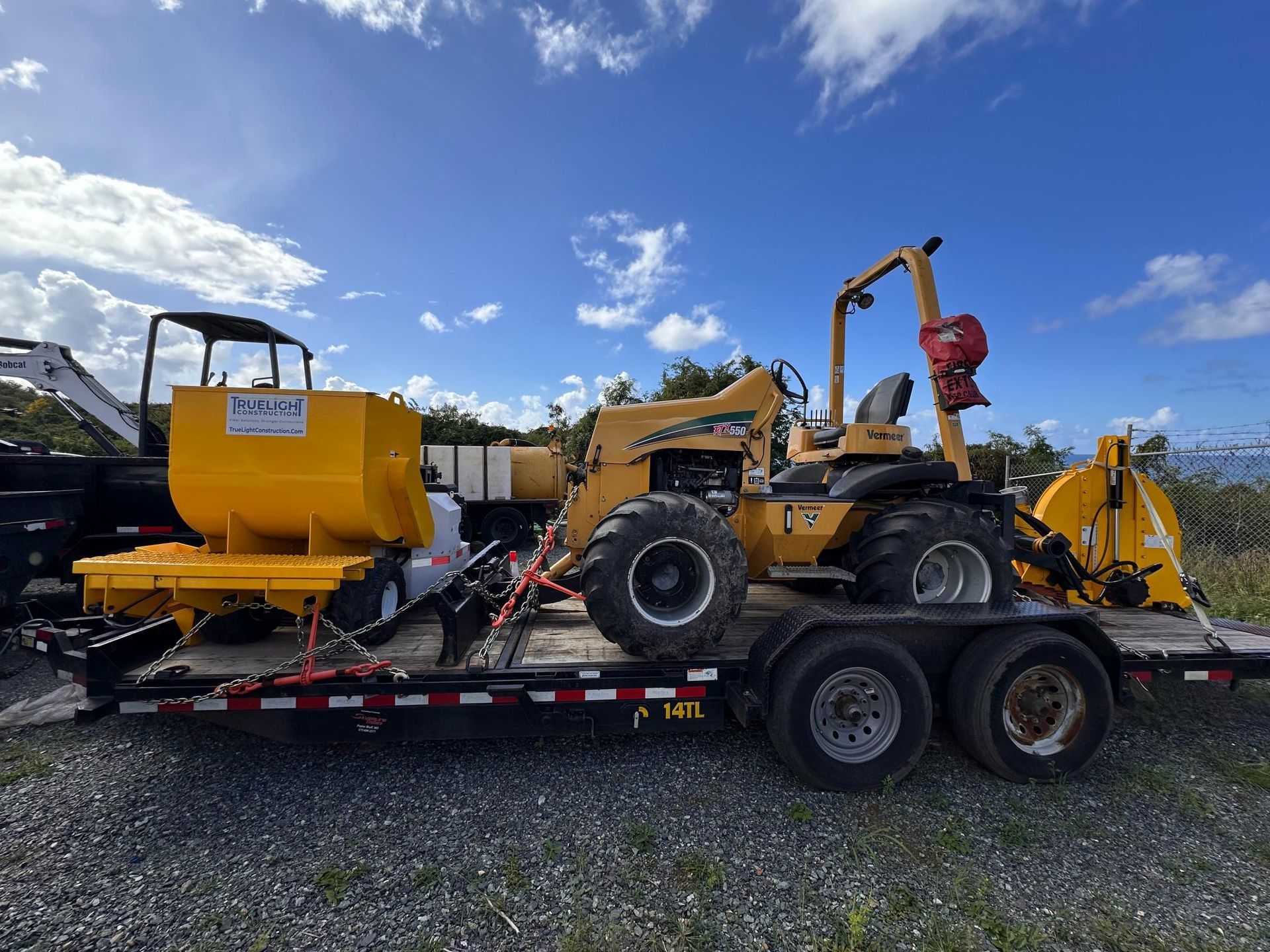 Yellow construction machinery on a flatbed trailer under a blue sky at an outdoor lot
