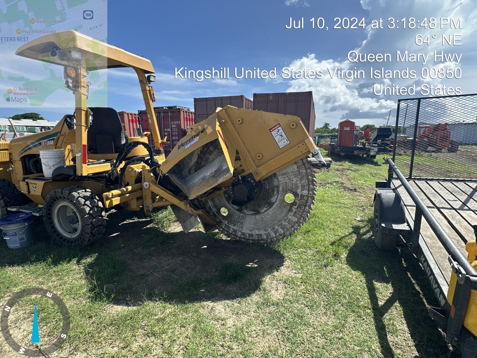 Yellow front loader lifting a dump trailer in a grassy lot under a blue sky