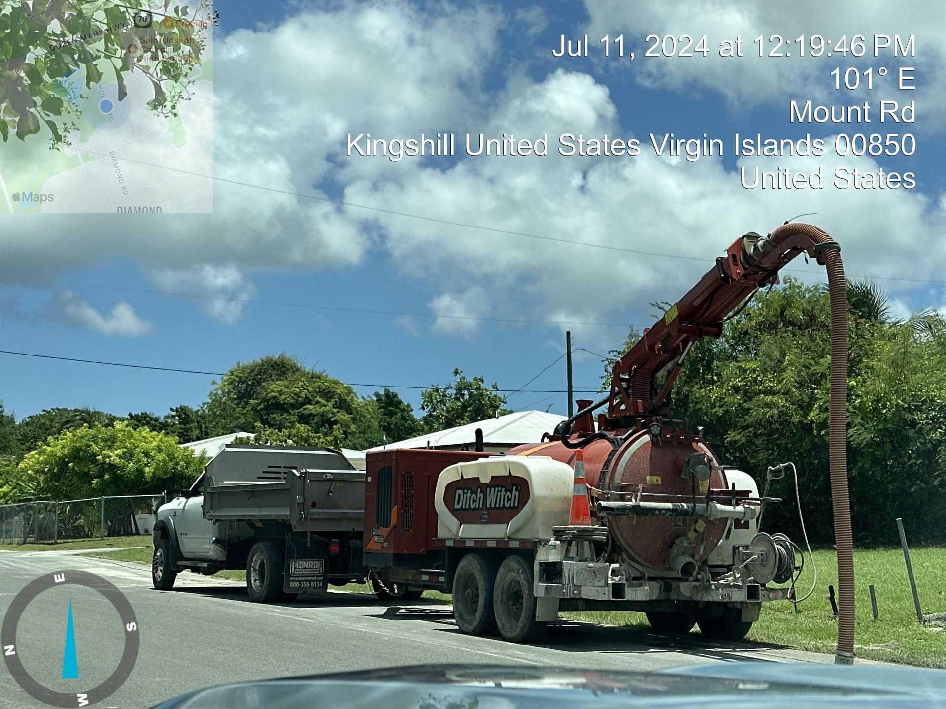 Red tow truck hauling a black car on a sunny road beside green grass and trees.