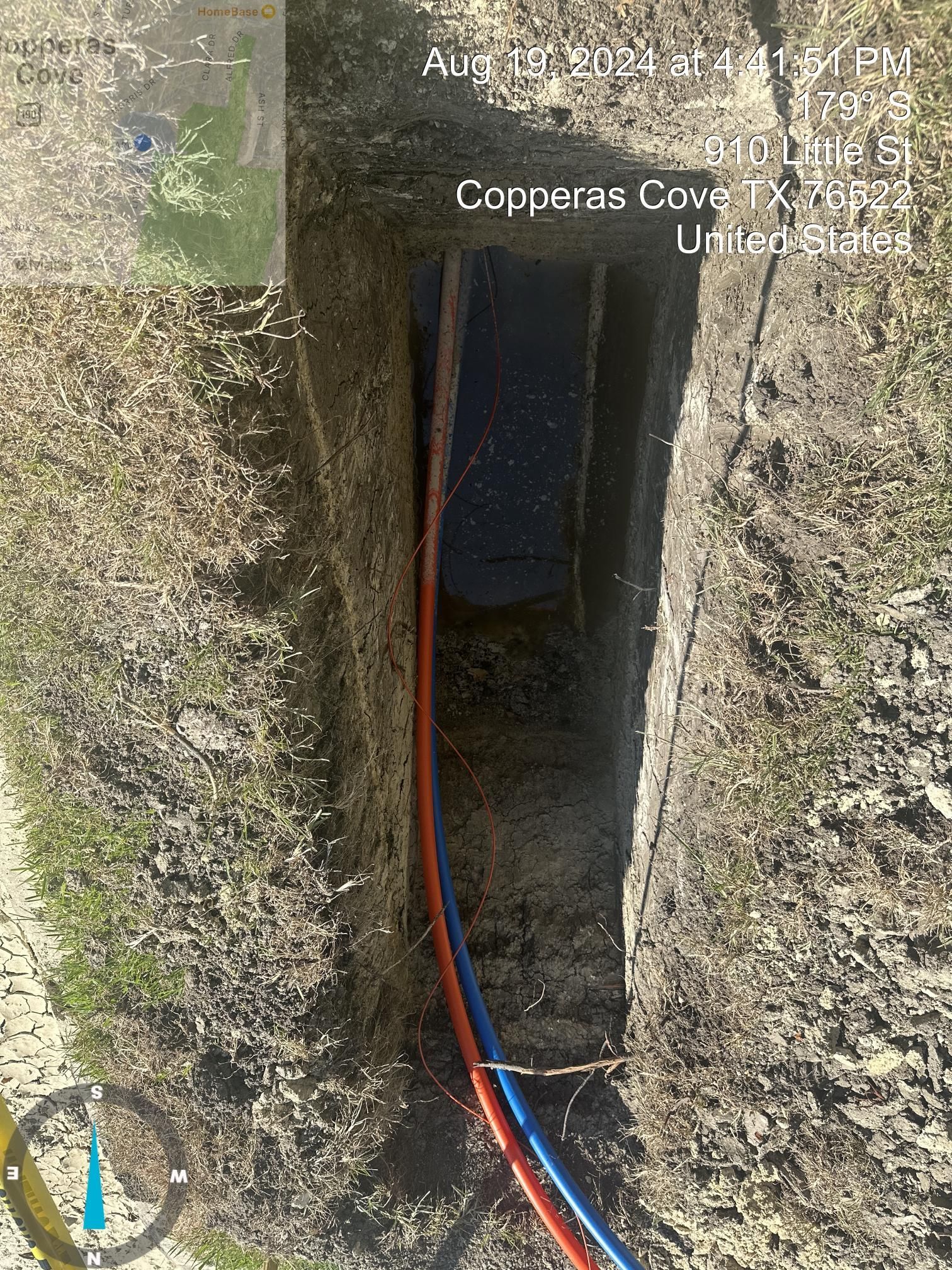 Water-filled trench with red and blue cables running into a narrow opening in the ground.