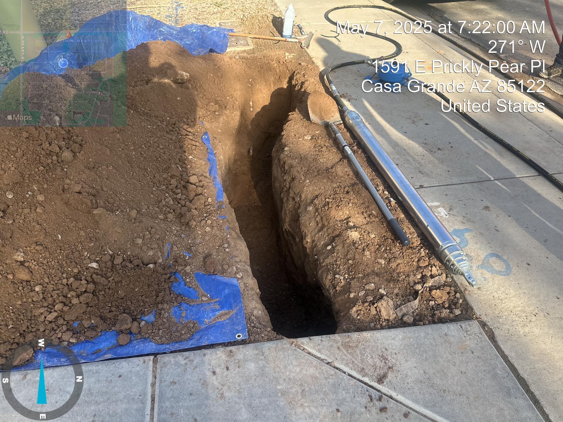 Large roadside excavation beside a sidewalk, with blue utility markings and an open trench near the curb