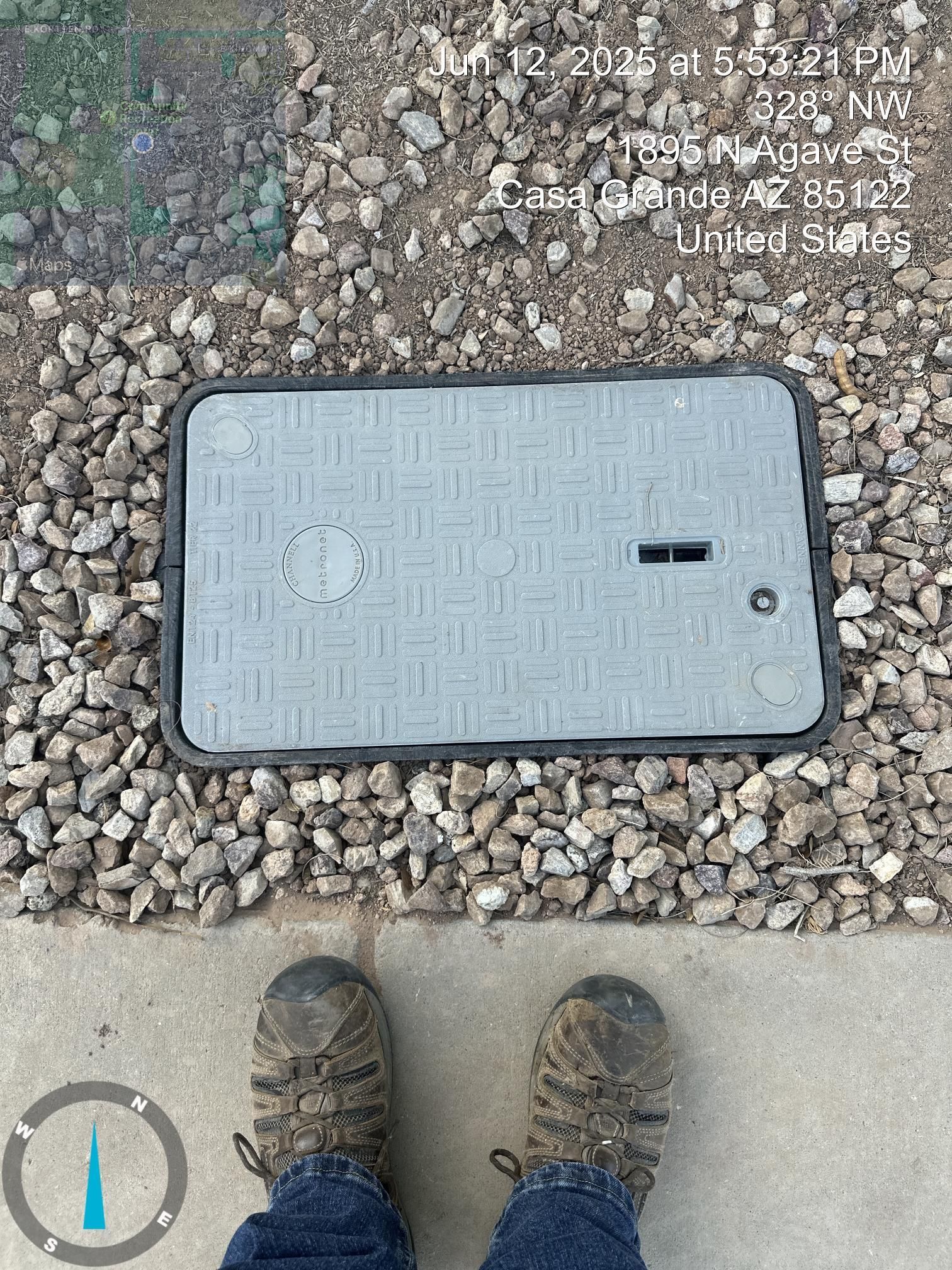 Gray utility box in gravel beside a sidewalk, with a person’s muddy shoes visible at the bottom.