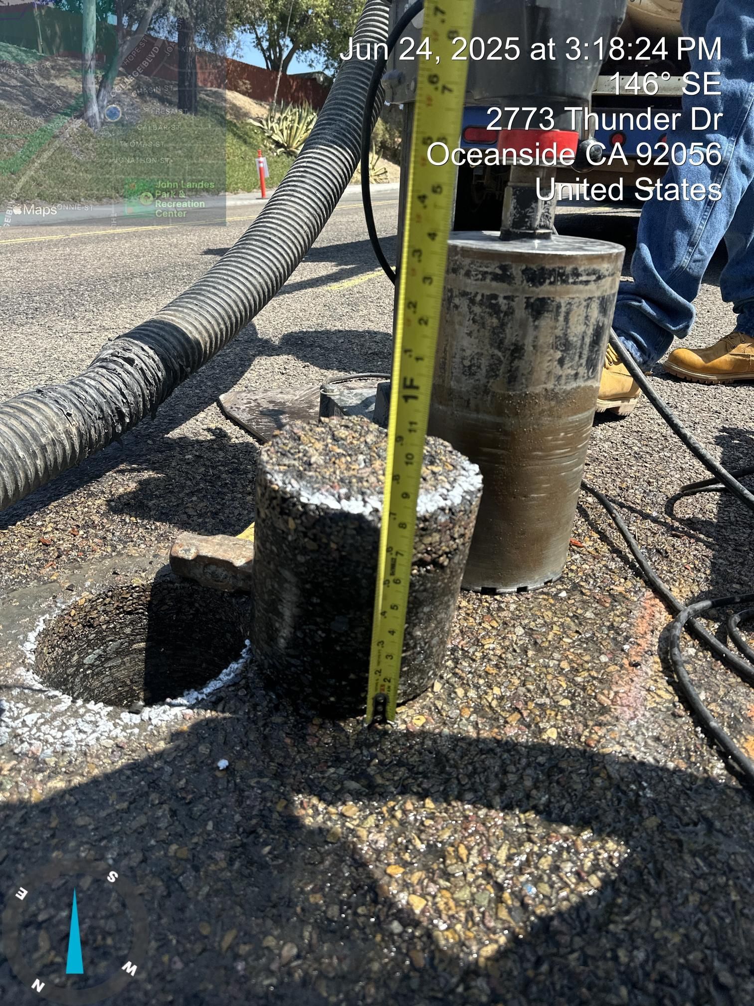 Concrete utility pedestal beside a yellow post and hose on wet pavement, with a measuring tape in the foreground