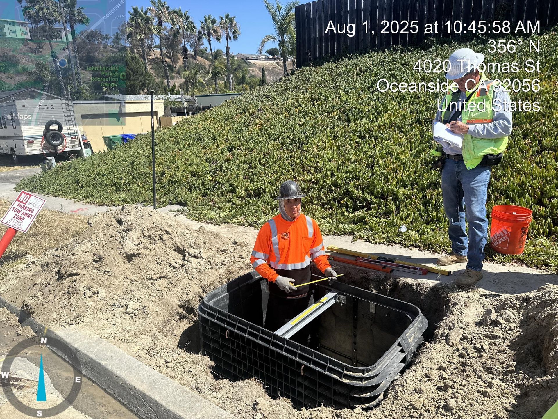 Workers install a utility box in a dirt trench at a roadside construction site