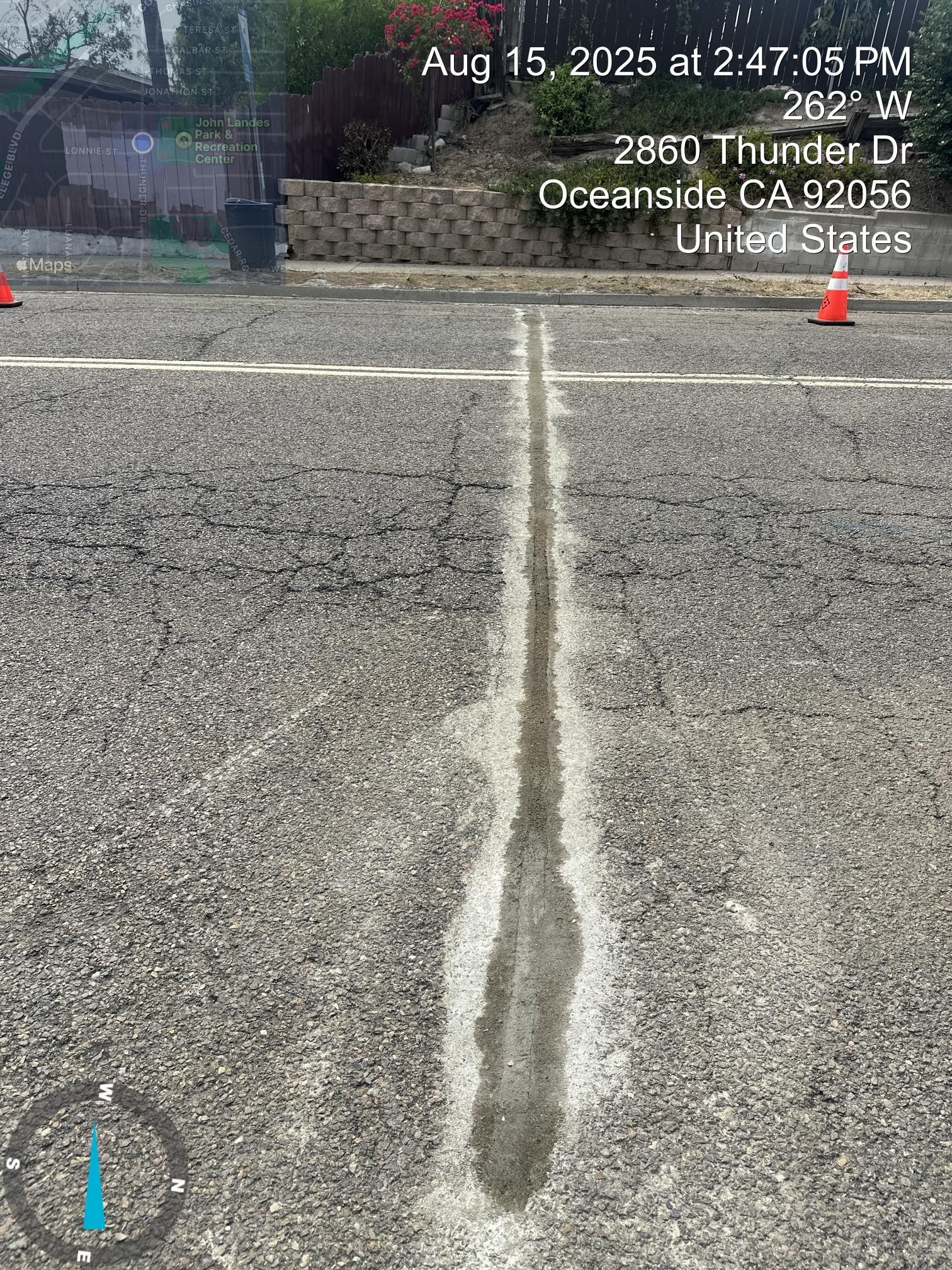 Cracked asphalt road with a long white seam down the center and faint street-view timestamp text.