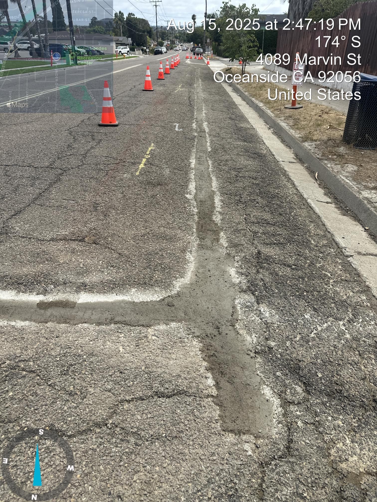 Cracked road under construction with orange traffic cones along the right lane.