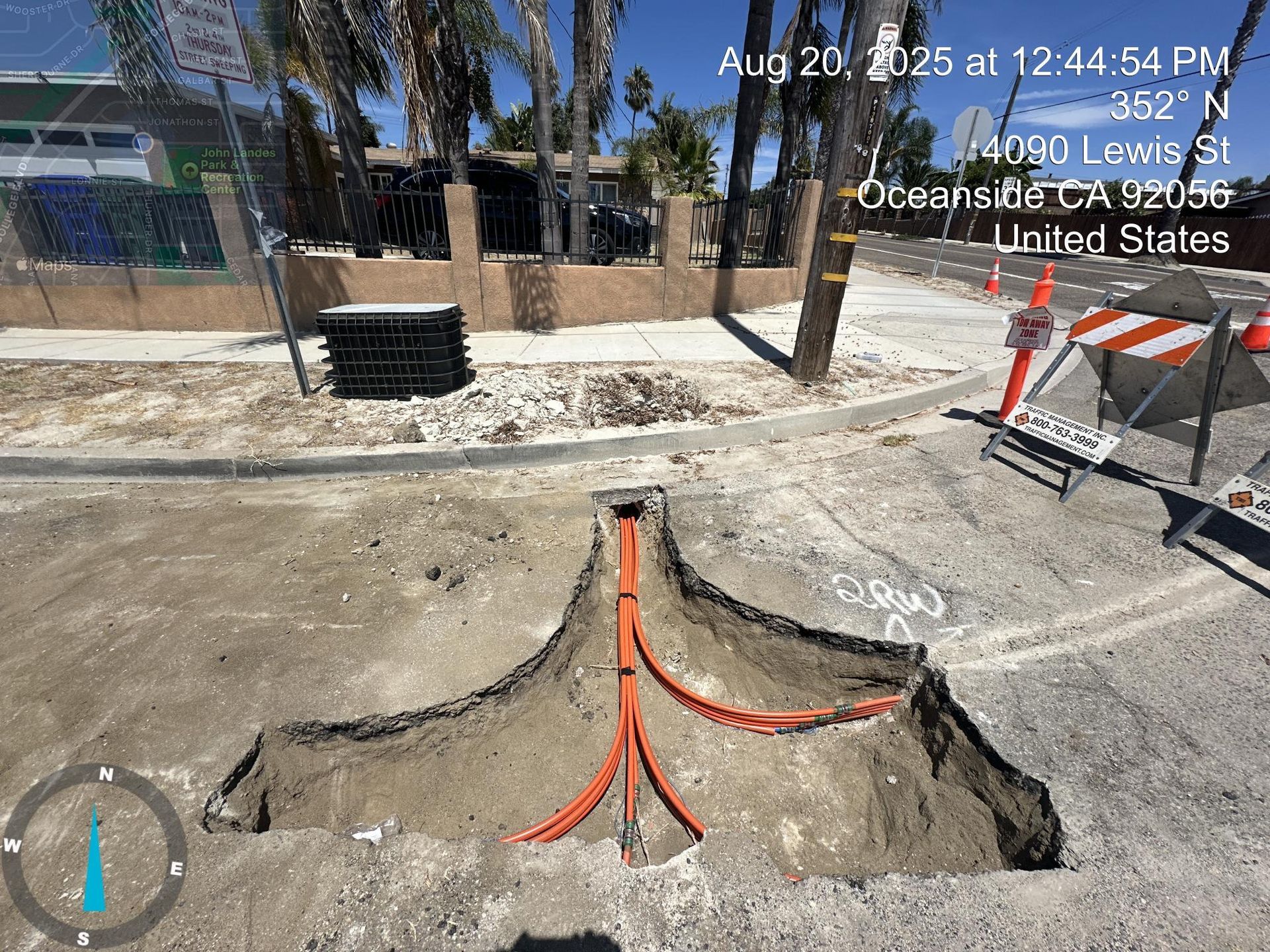 Orange utility pipes in a concrete excavation beside a building and a sidewalk