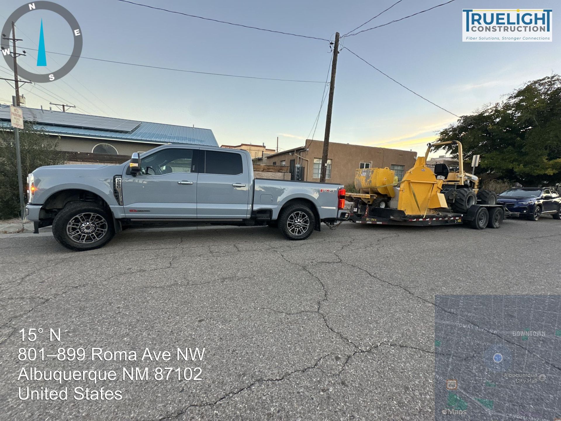 Silver pickup towing yellow street sweeper on a road in Albuquerque, New Mexico, with damage visible nearby