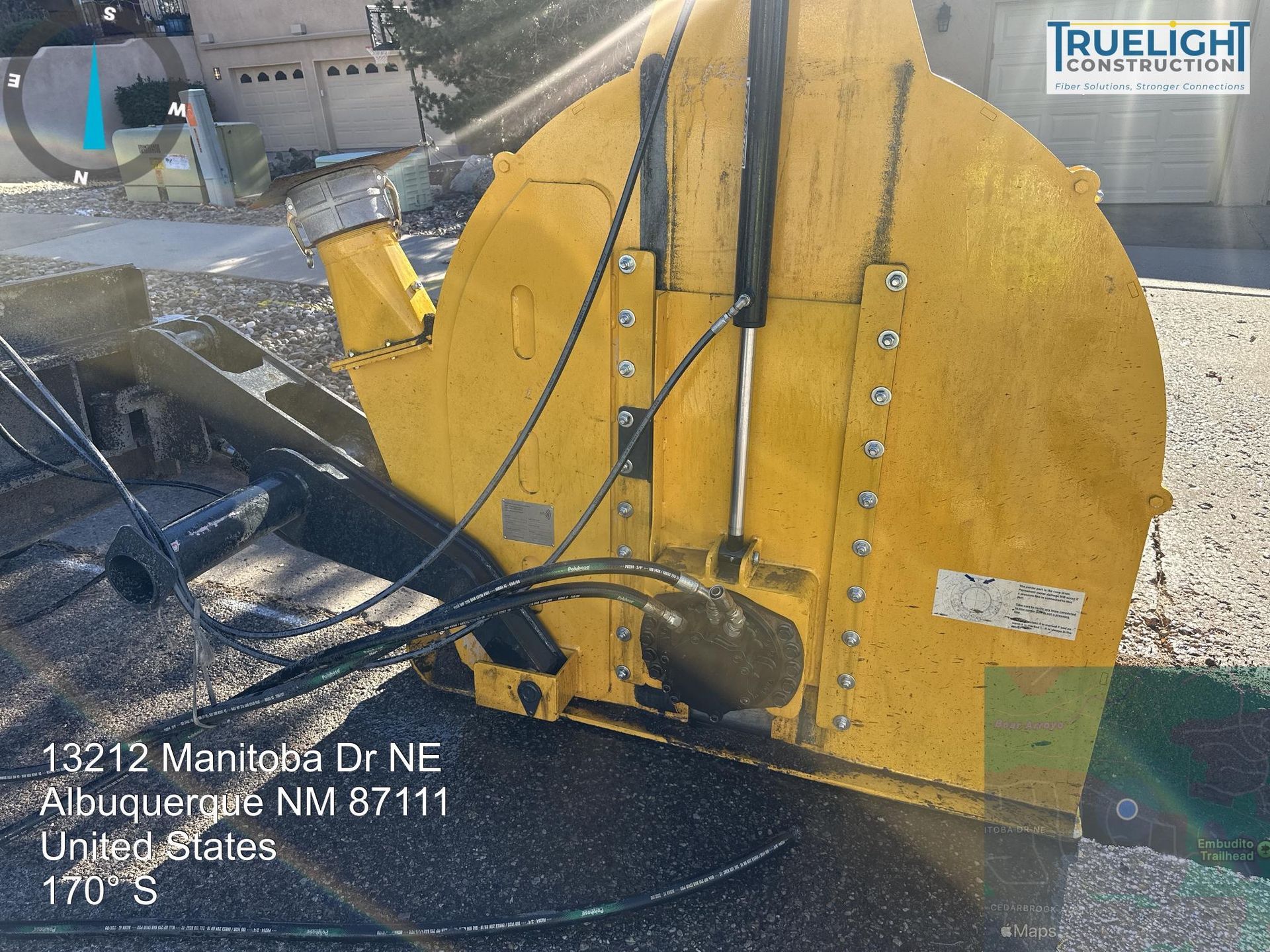 Yellow snowplow blade attached to a truck at a snowy intersection, with a TRUELIGHT logo visible.