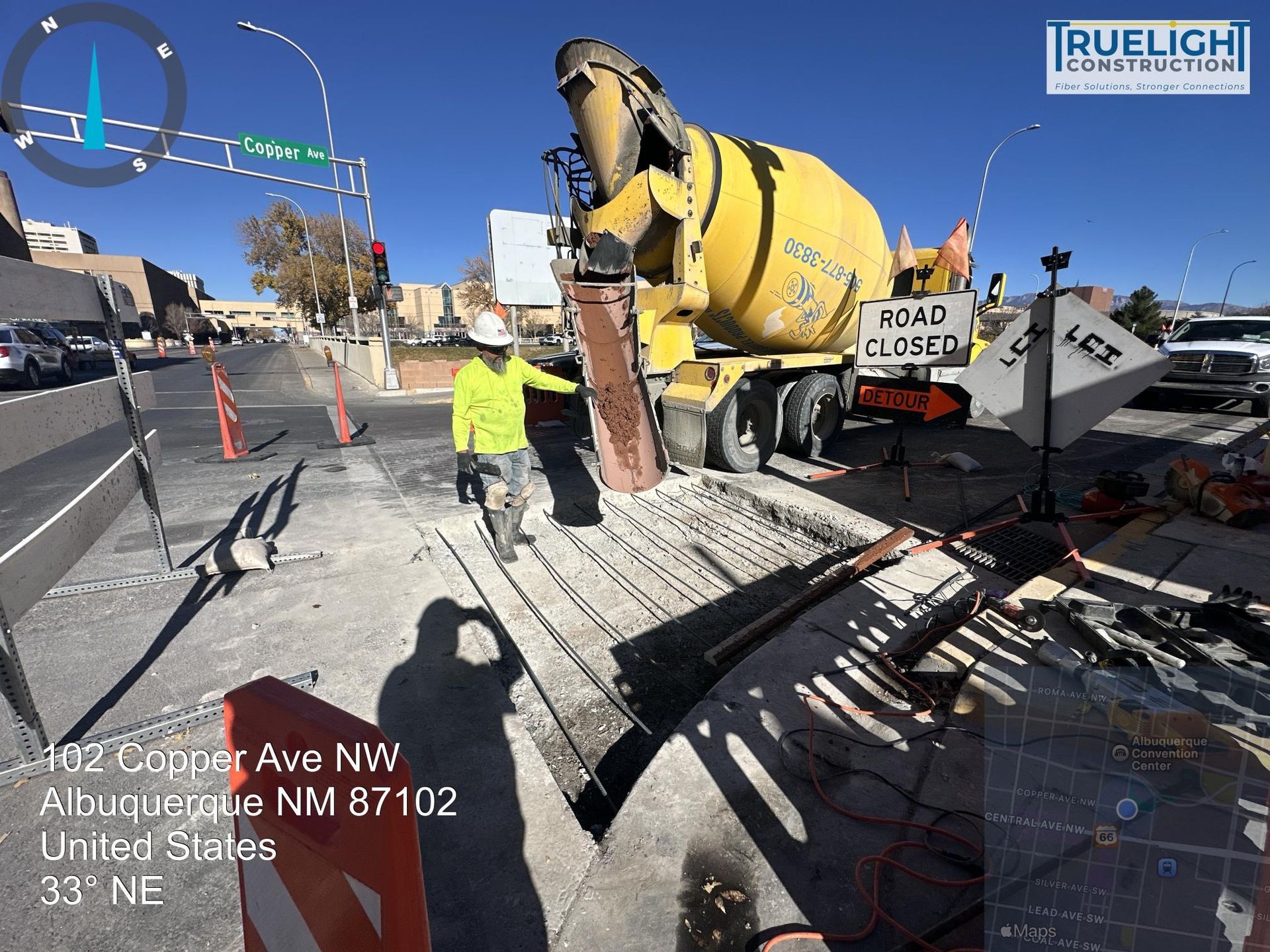 Construction workers pouring concrete beside a yellow cement mixer on a city street