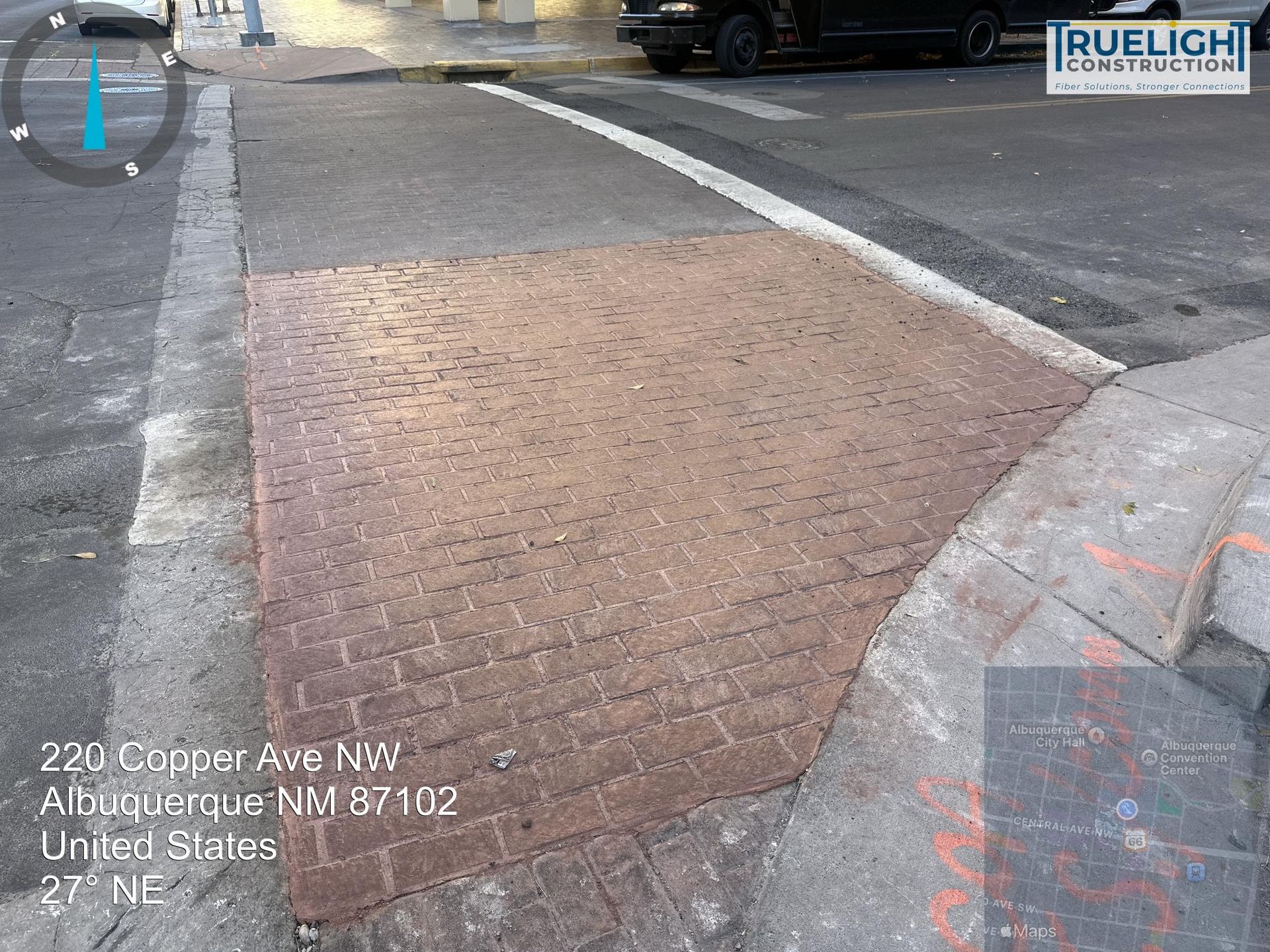 Sidewalk curb ramp with textured brick pavement at a street corner, next to a crosswalk and road