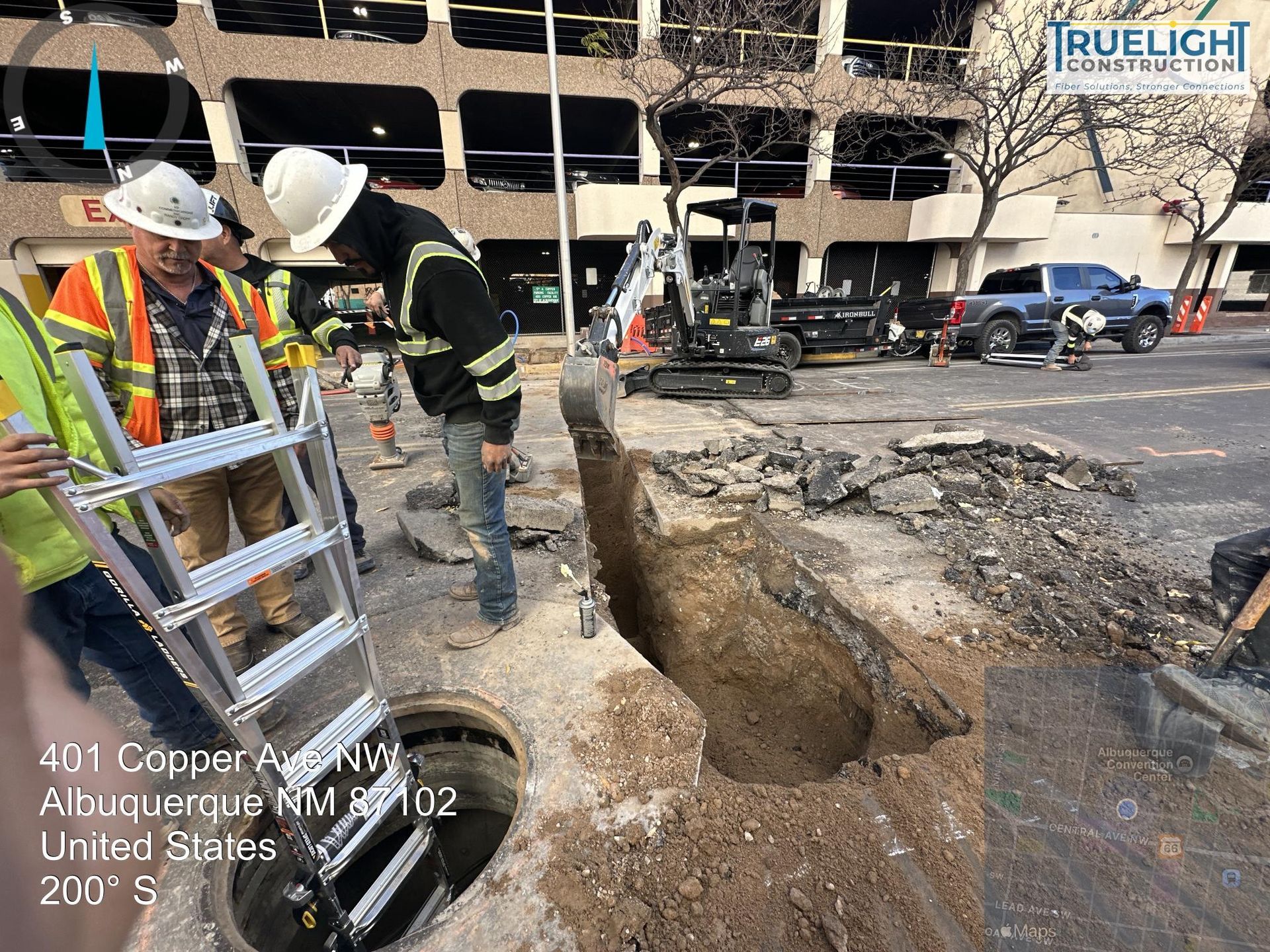 Workers and utility trucks around a large sinkhole on a city street next to a building.
