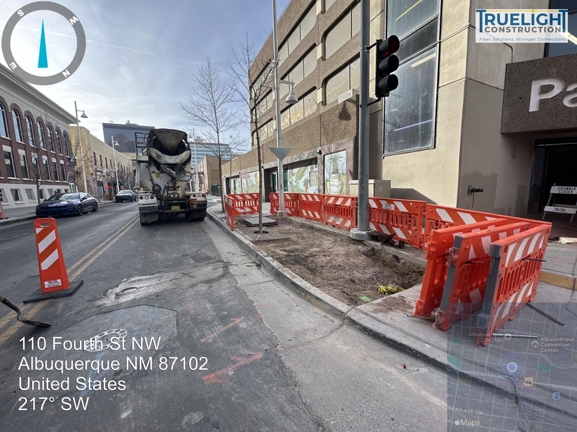 Roadwork with orange barriers beside a street in New York City, a cement truck ahead.