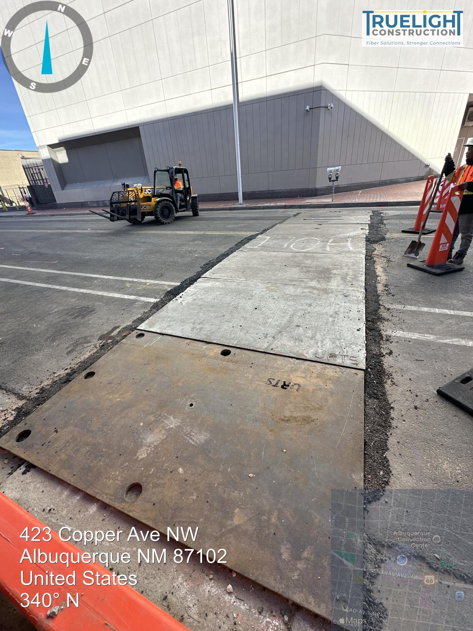 Construction area outside a gray warehouse, with a forklift, cones, and a cracked concrete sidewalk under repair.