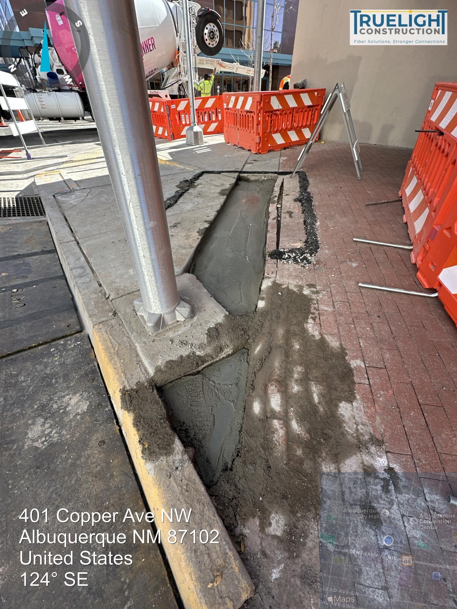 Construction site with metal pole, orange barriers, and uneven concrete sidewalk by curb cut