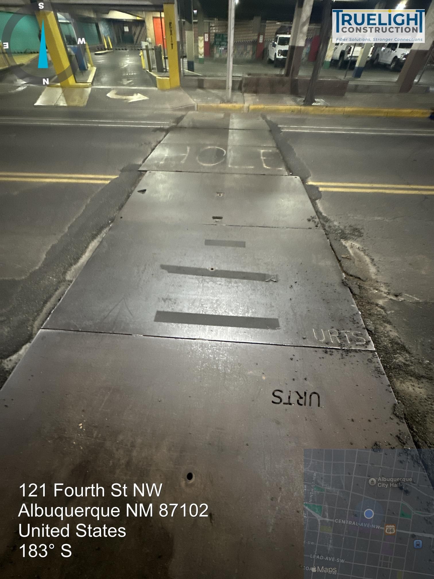Street crossing with a worn concrete ramp at night, viewed toward a building entrance.