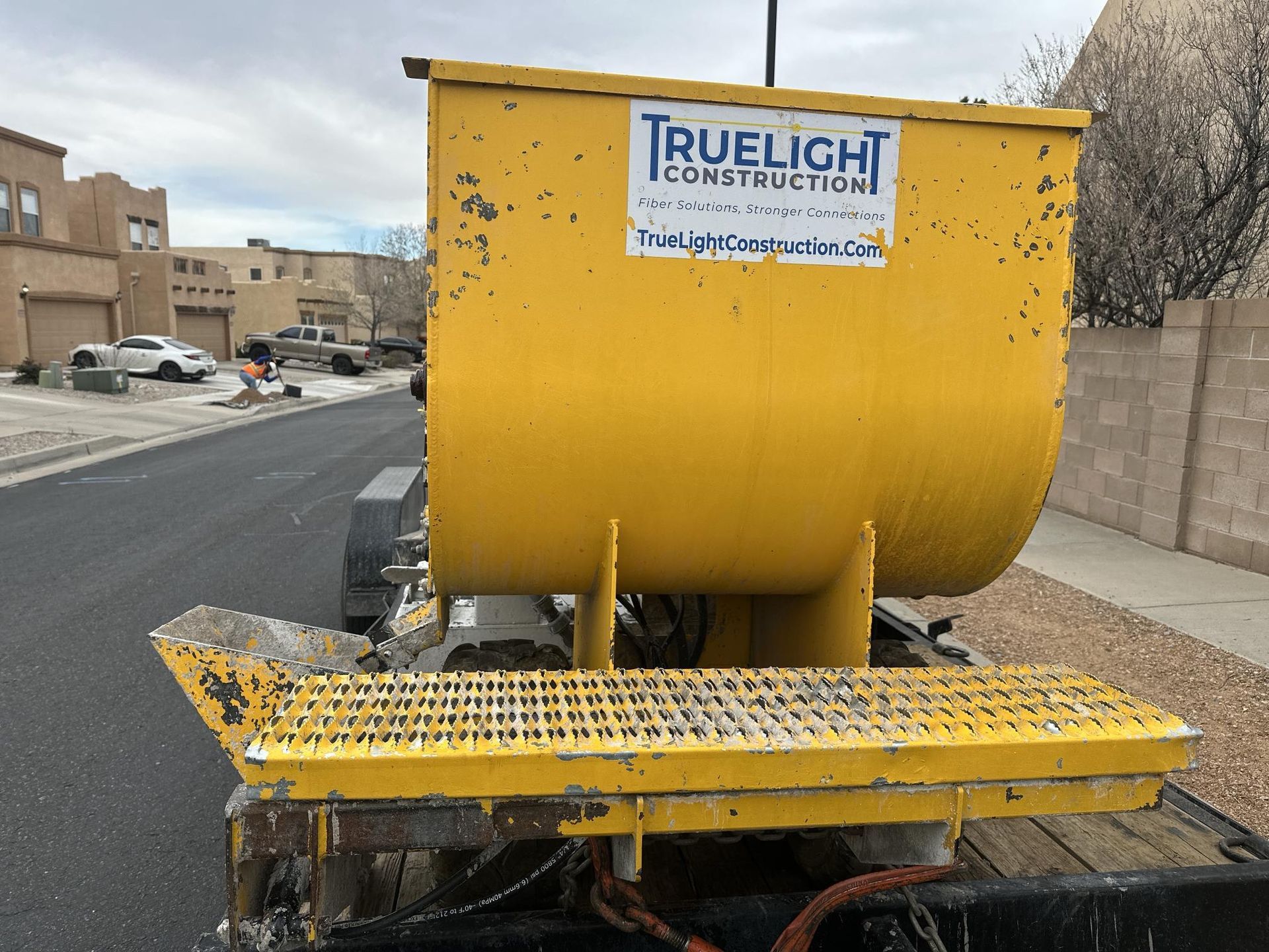 Yellow construction hopper trailer with “Truelight Construction” sign parked on a street.