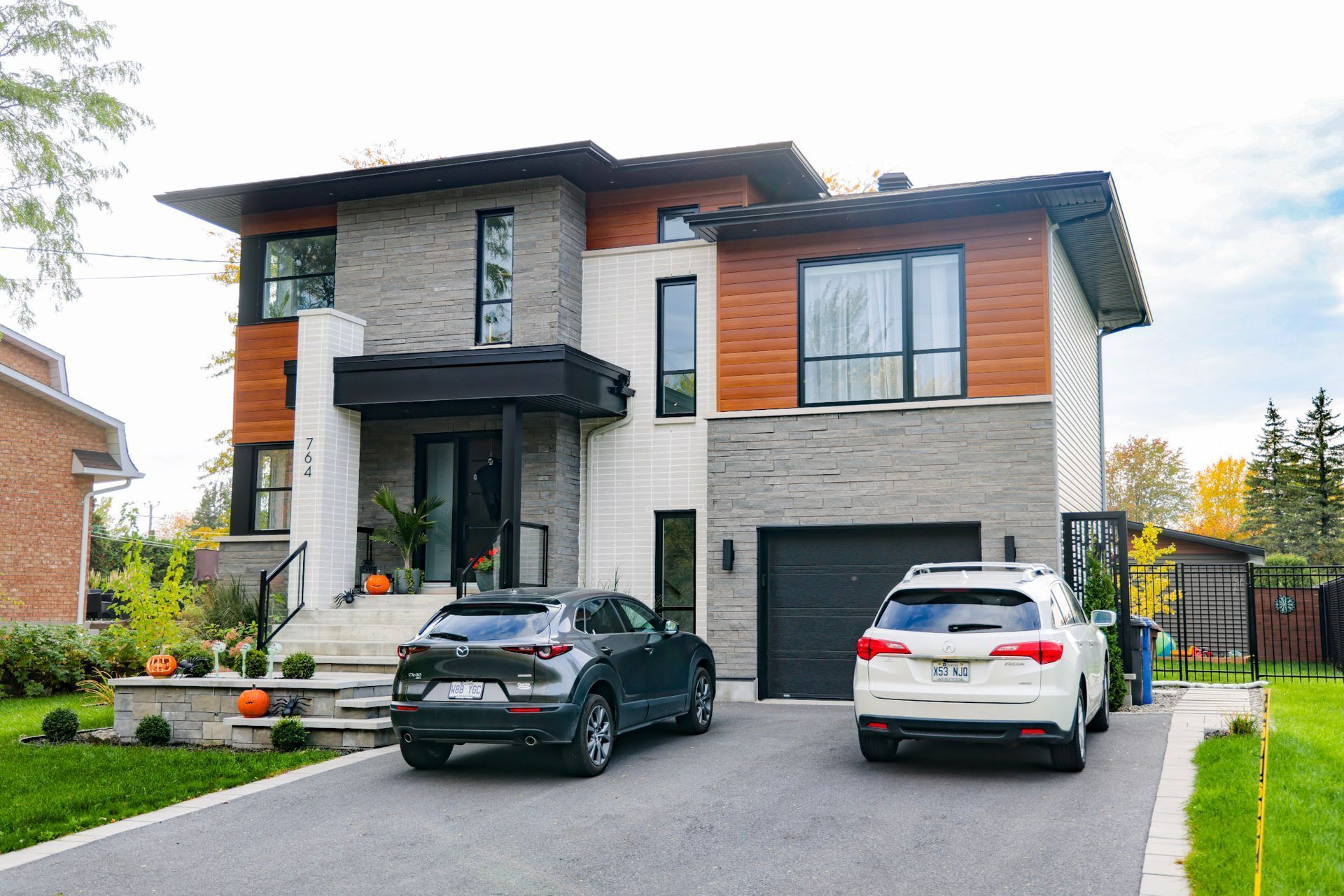 Maison moderne à deux étages avec extérieur en pierre et en bois, deux voitures garées dans l'allée.