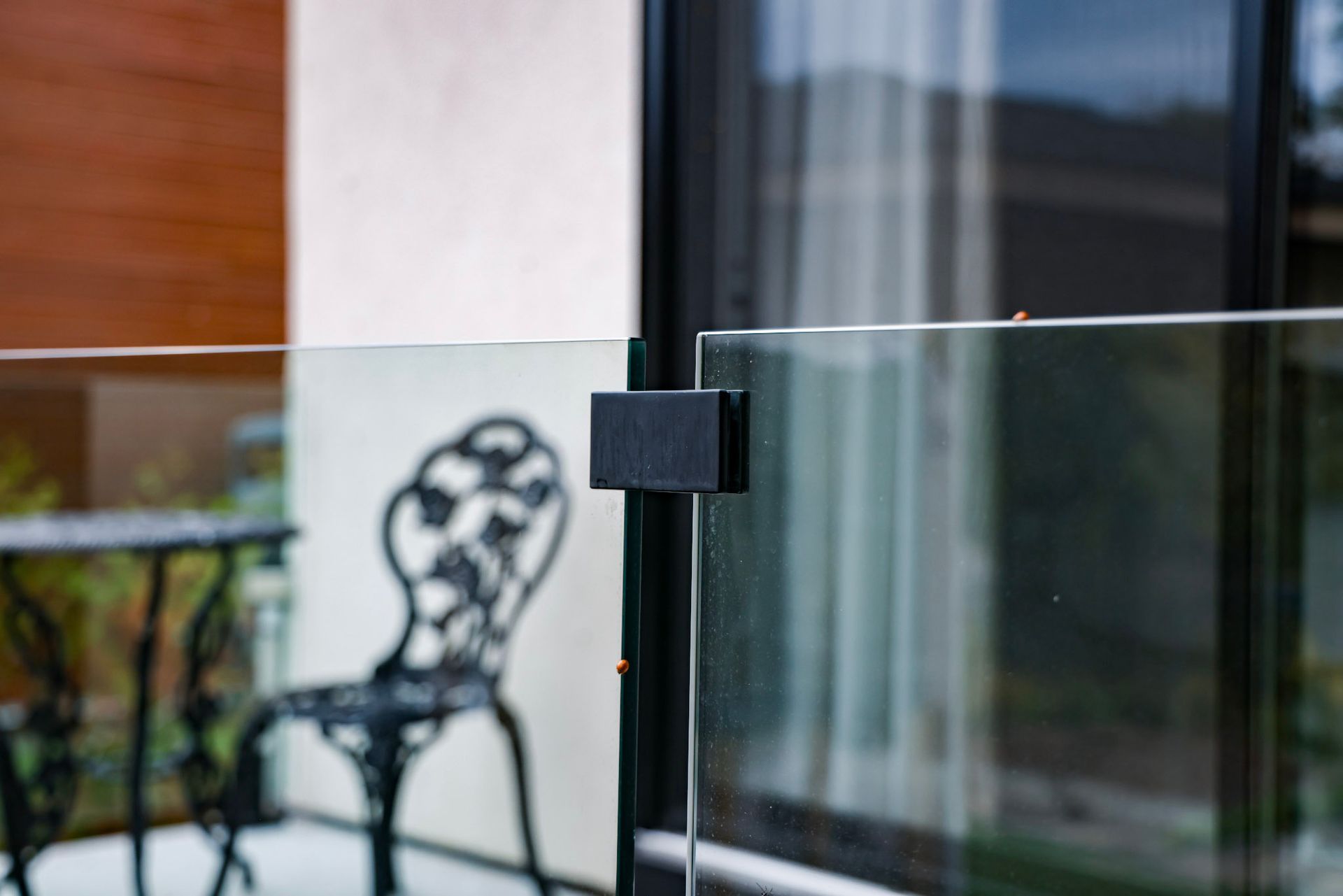 Rambarde de balcon en verre avec une pince en métal noir et chaise de patio floue en arrière-plan