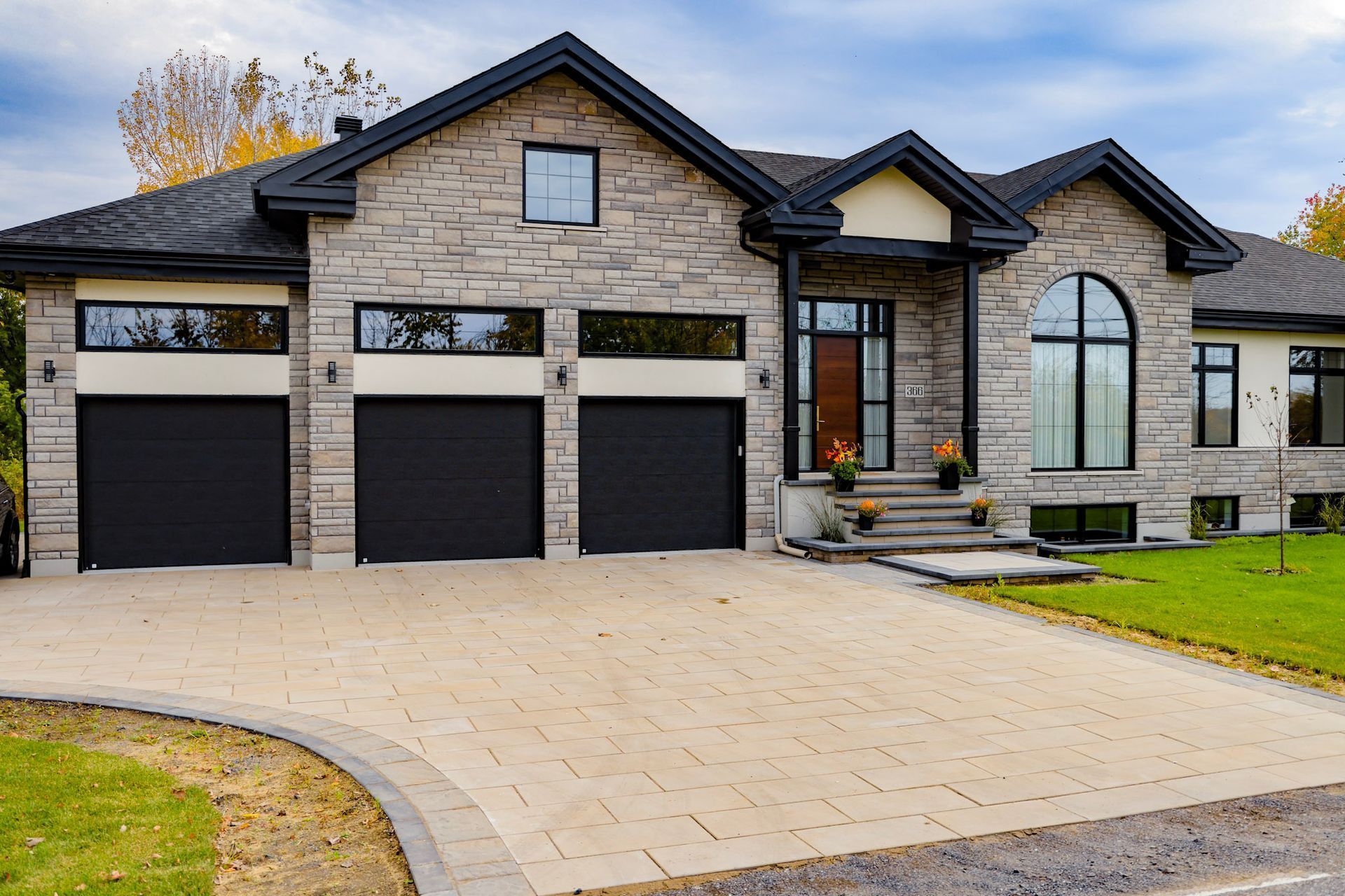 Maison moderne en briques avec trois portes de garage et une allée pavée