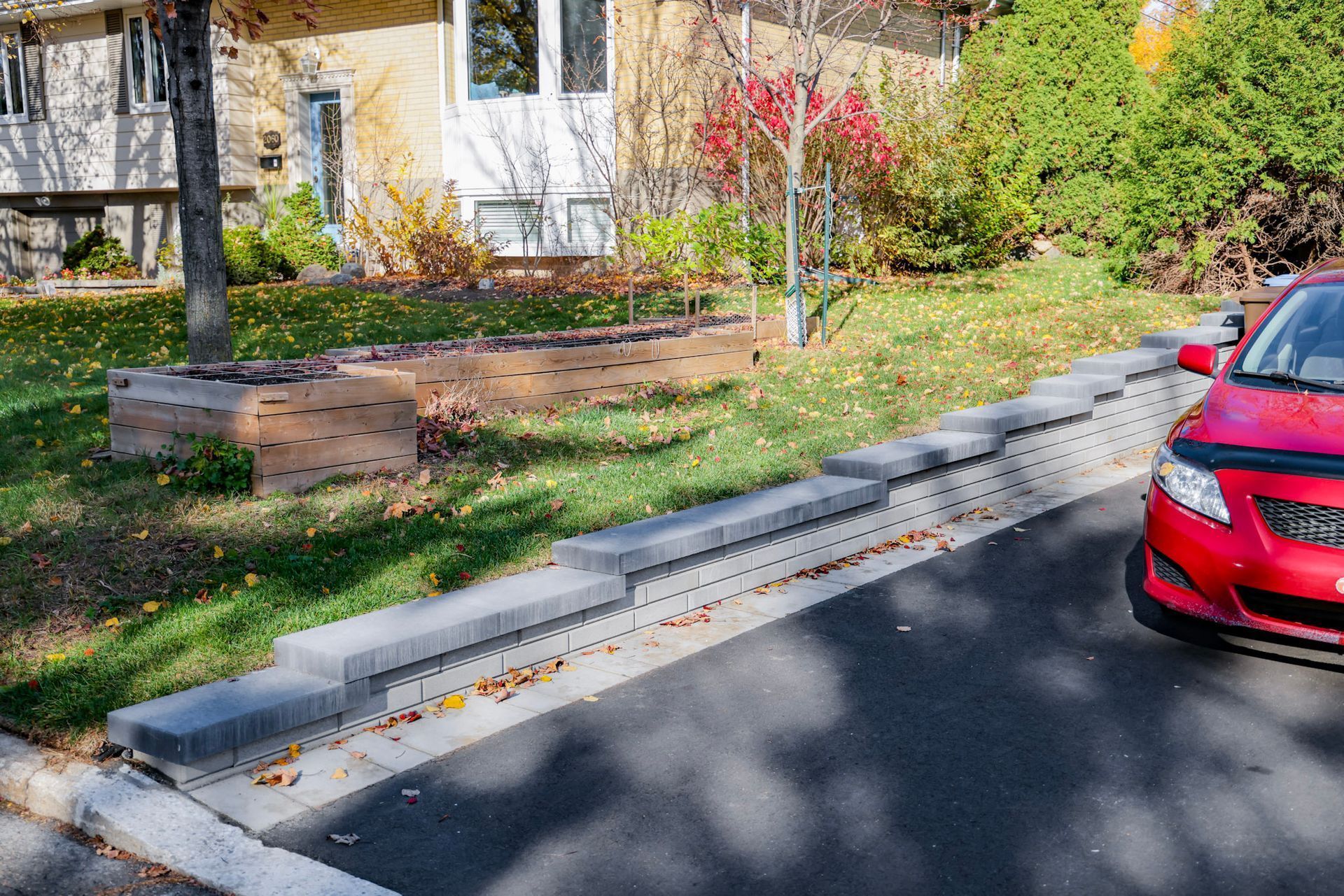 Rampe d'accès en béton au bord d'une route, avec une voiture rouge garée à droite et un bâtiment et des arbres en arrière-plan.