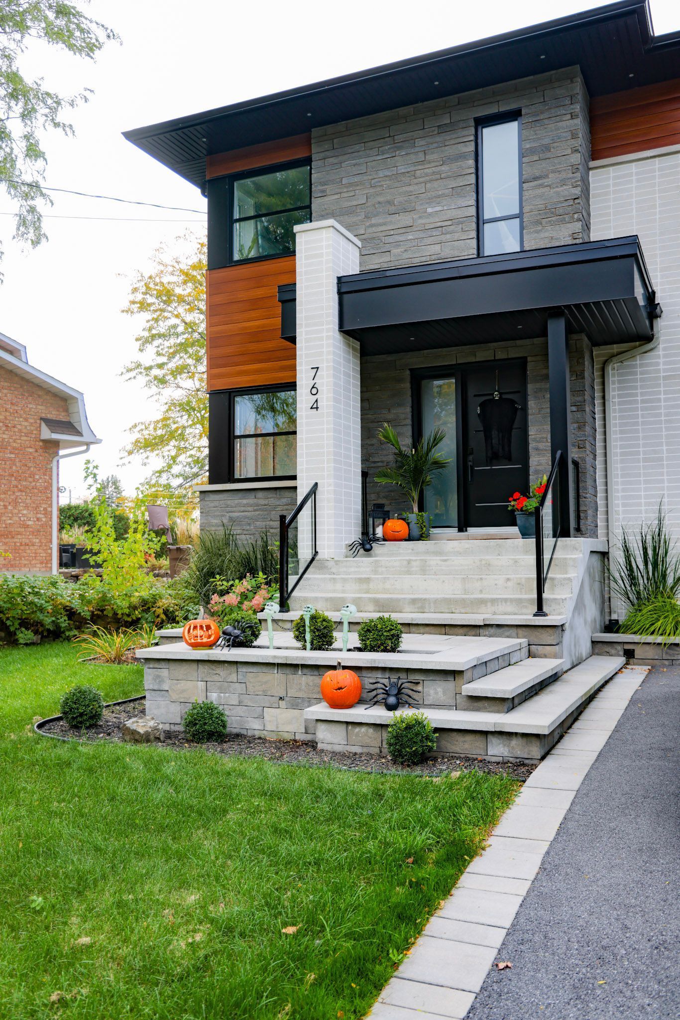 Maison moderne à deux étages avec perron, façade en briques blanches, auvent noir et citrouilles orange sur le porche.