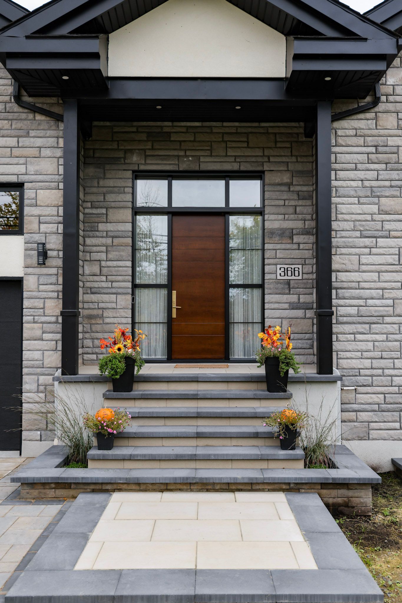 Entrée principale d'une maison moderne en pierre avec marches, porte en bois et pots de fleurs orange de chaque côté